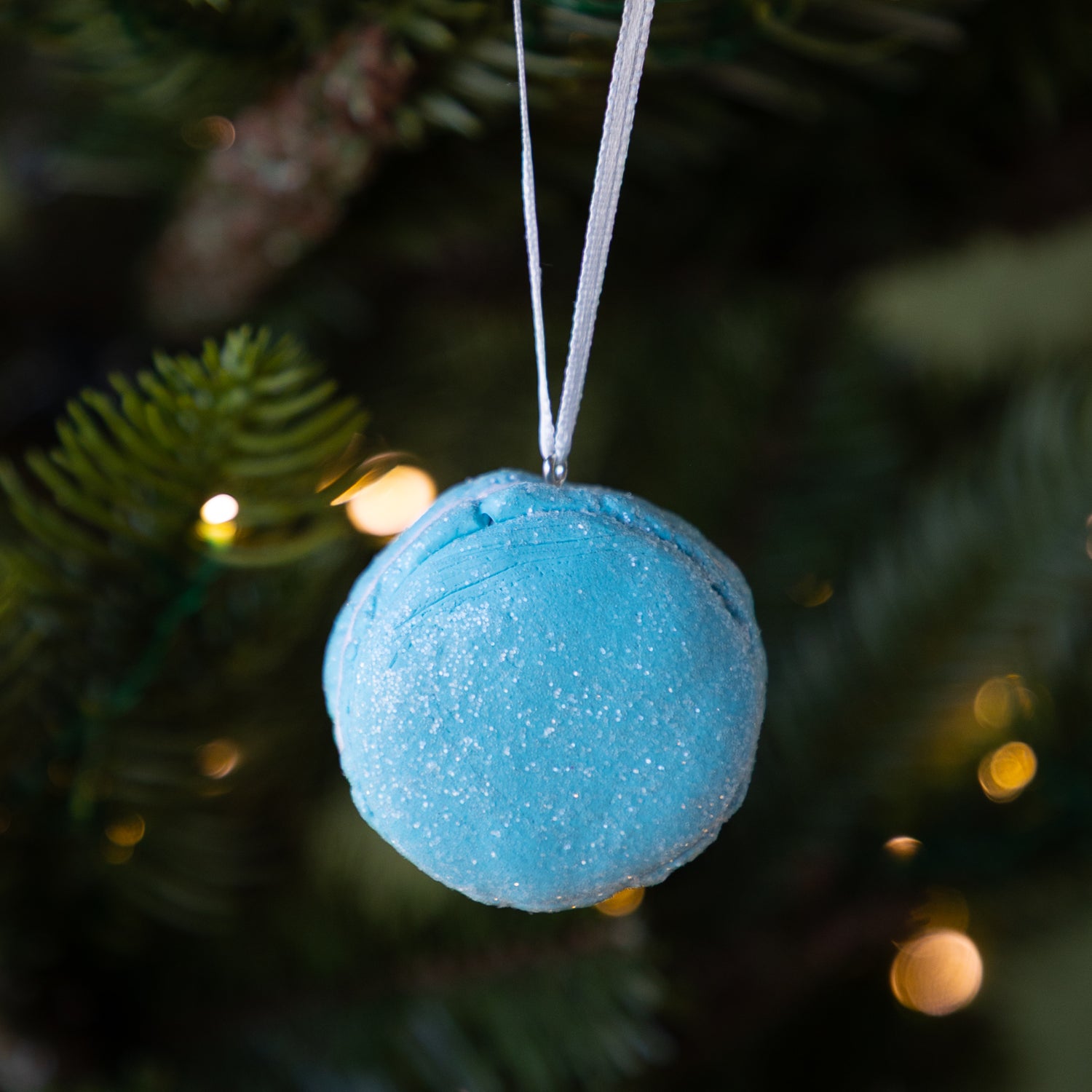 Blue macaron ornament hanging on a Christmas tree with blurred lights in the background.