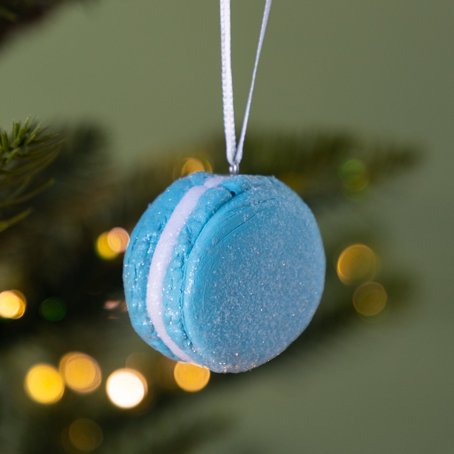 Blue macaron ornament hanging on a Christmas tree with blurred lights in the background.