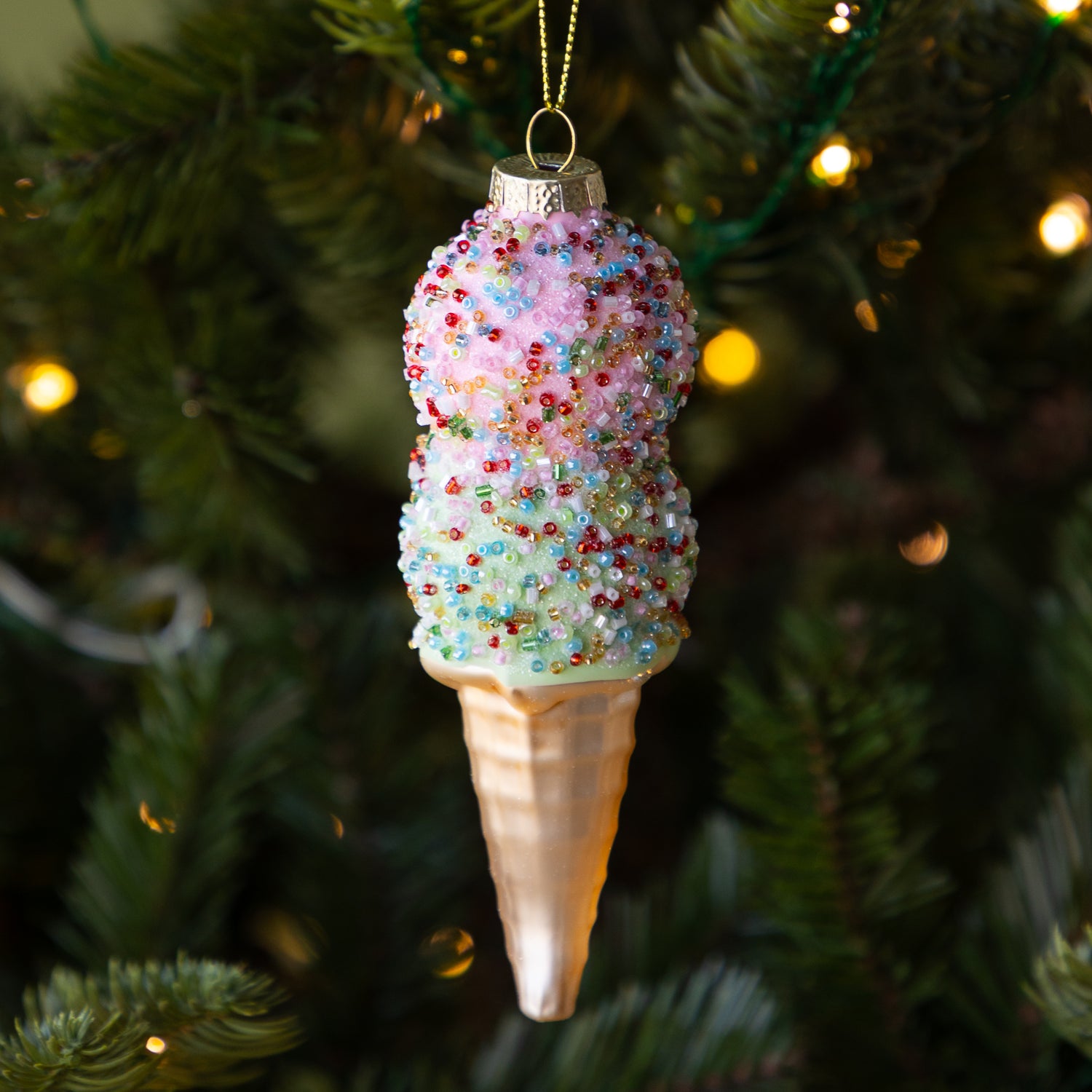 Decorative ice cream cone ornament with colorful sprinkles on a Christmas tree.