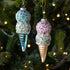 Two ice cream cone ornaments with colorful sprinkles hanging on a Christmas tree.