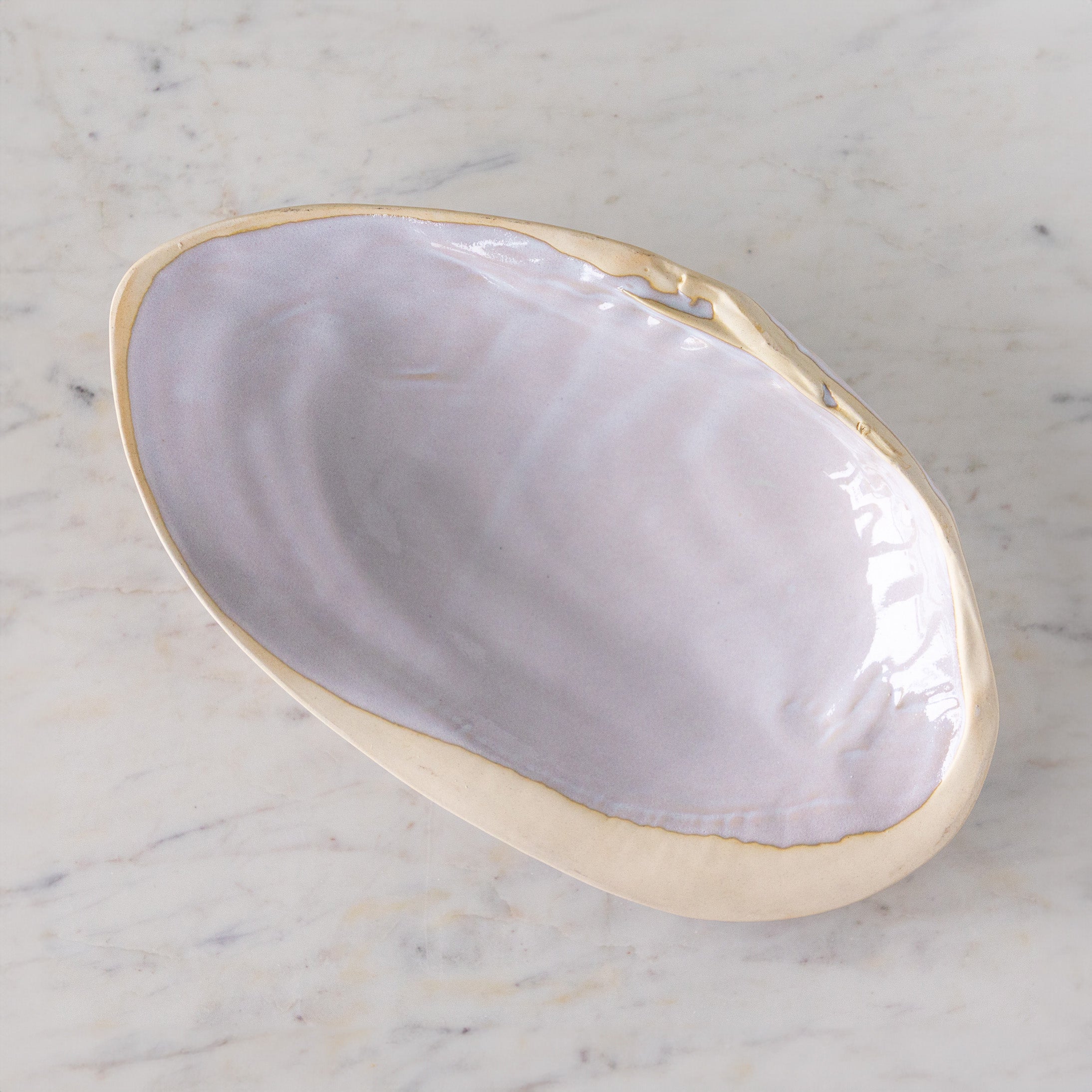 A large, oyster shell shaped dish with white reactive glaze, on a marble table.