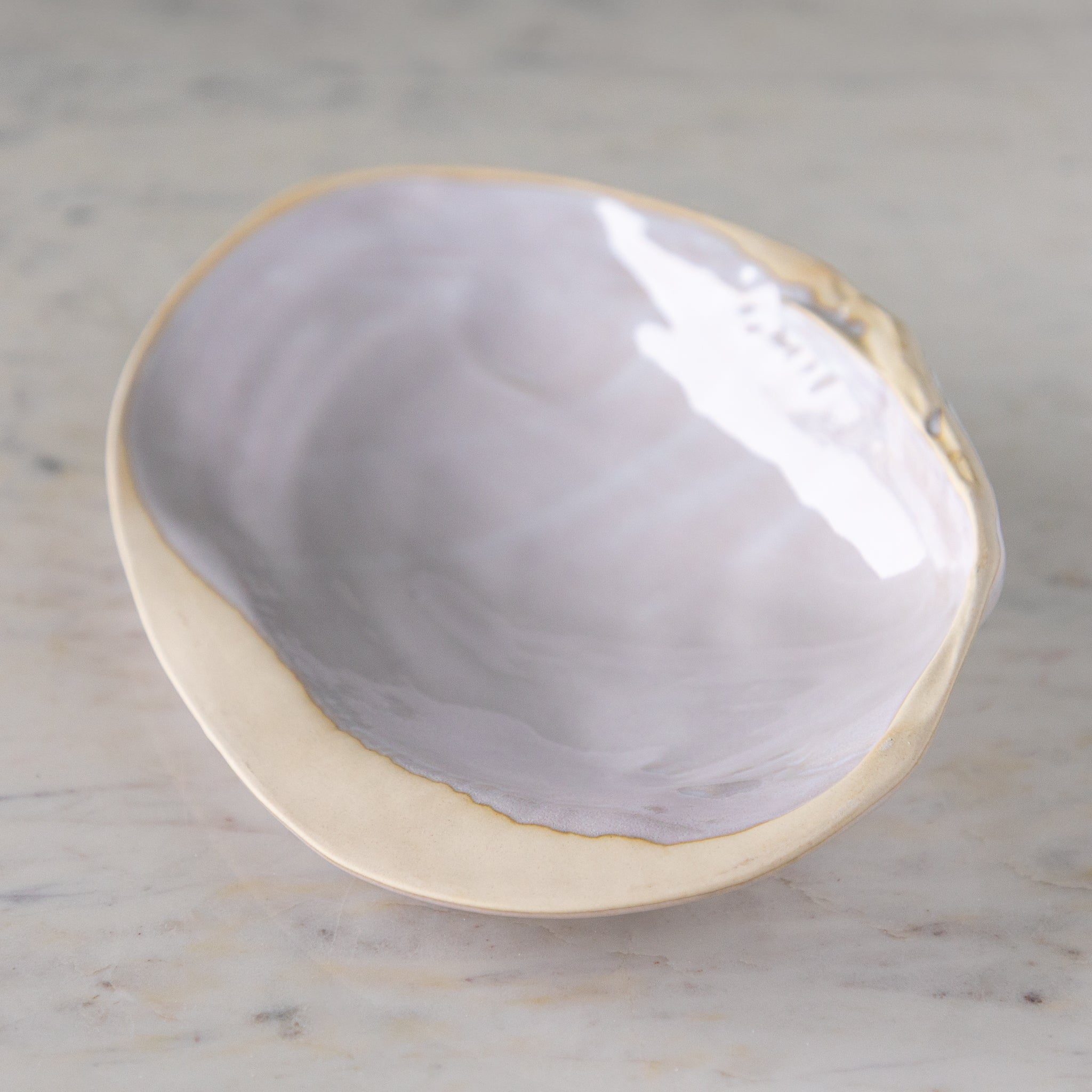 A large, oyster shell shaped dish with white reactive glaze, on a marble table.