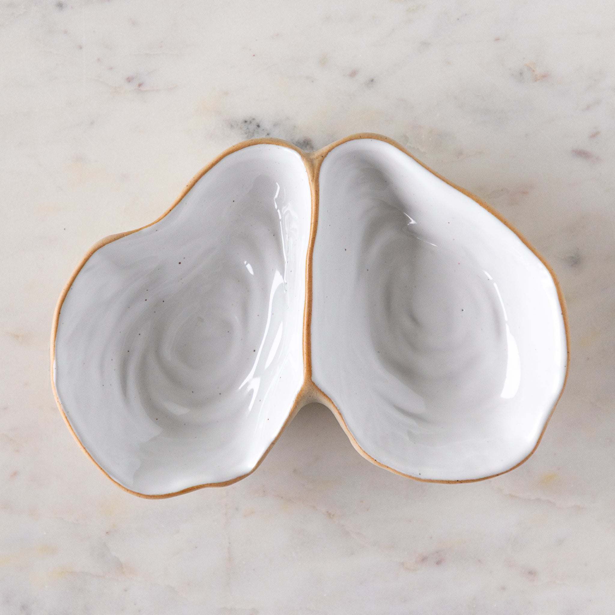 An open oyster shaped dish with white reflective glaze on the inside, on a marble table.