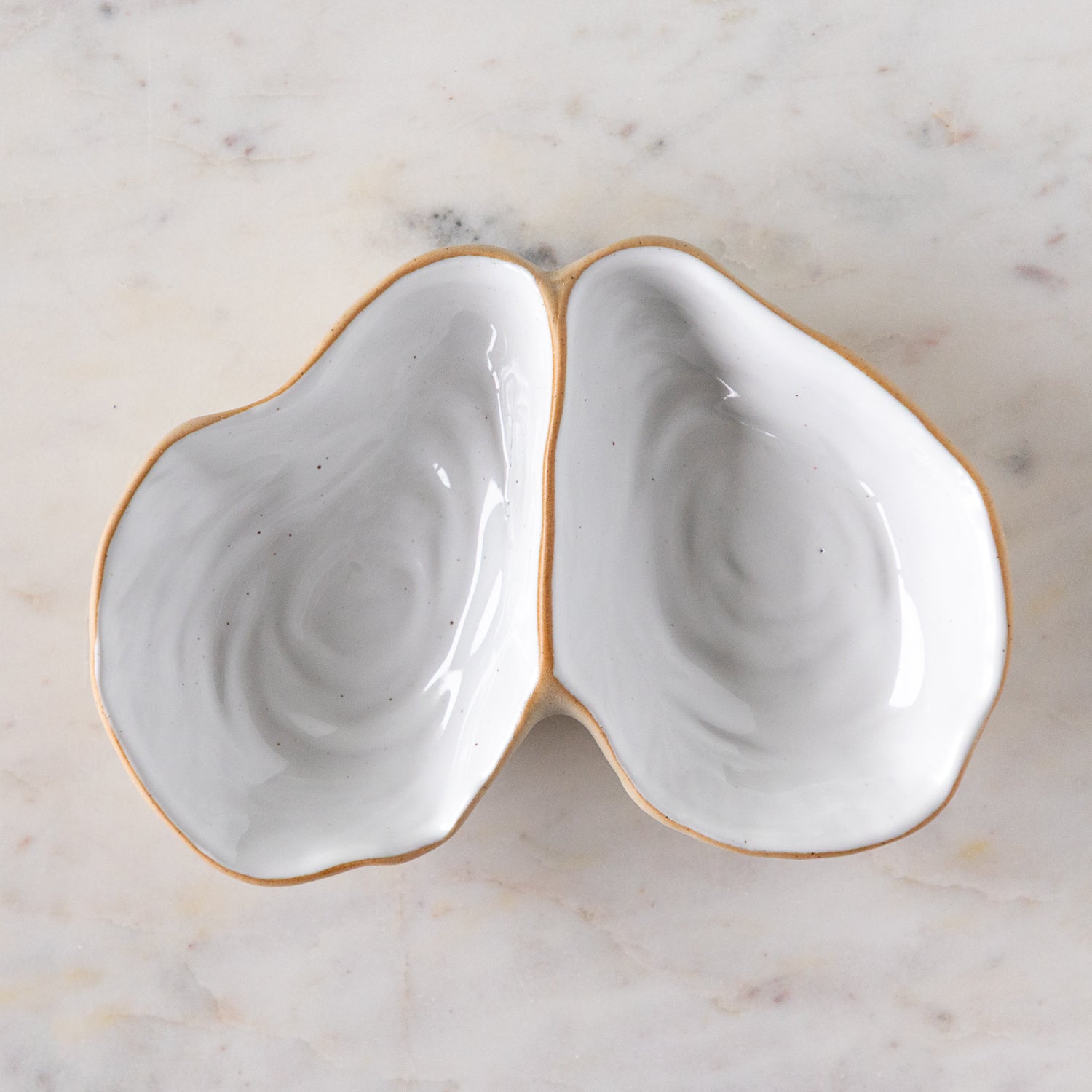 An open oyster shaped dish with white reflective glaze on the inside, on a marble table.