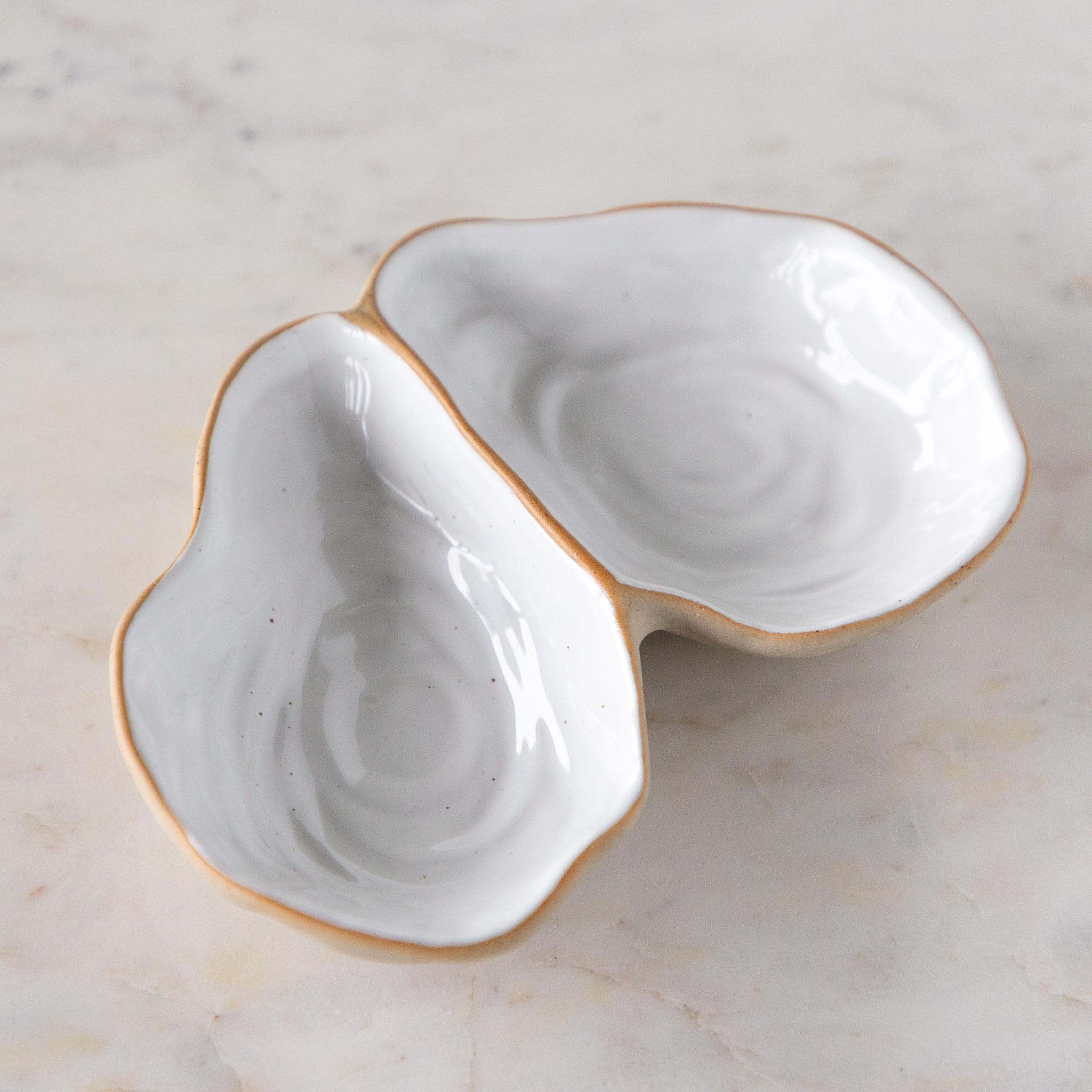 An open oyster shaped dish with white reflective glaze on the inside, on a marble table.