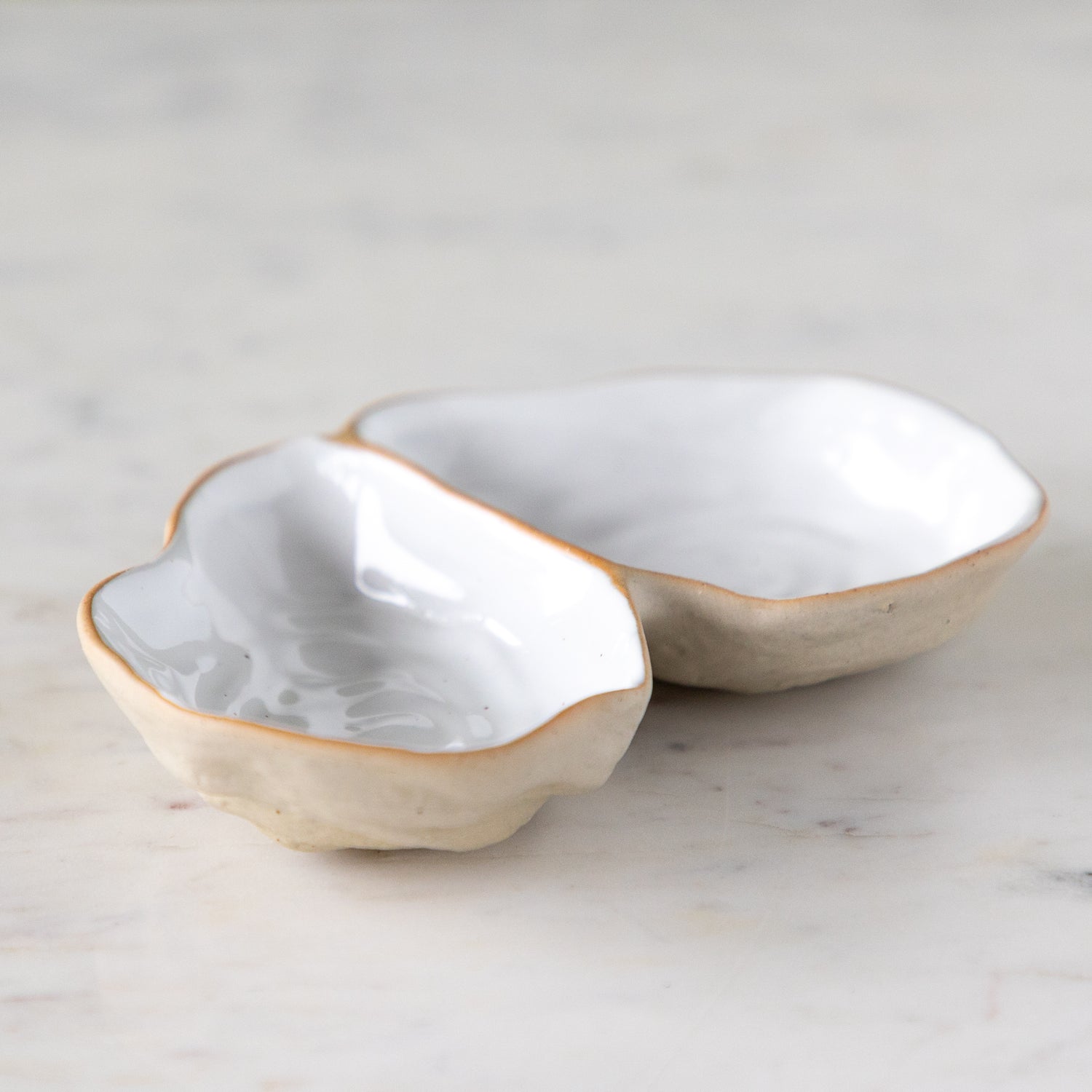 An open oyster shaped dish with white reflective glaze on the inside, on a marble table.