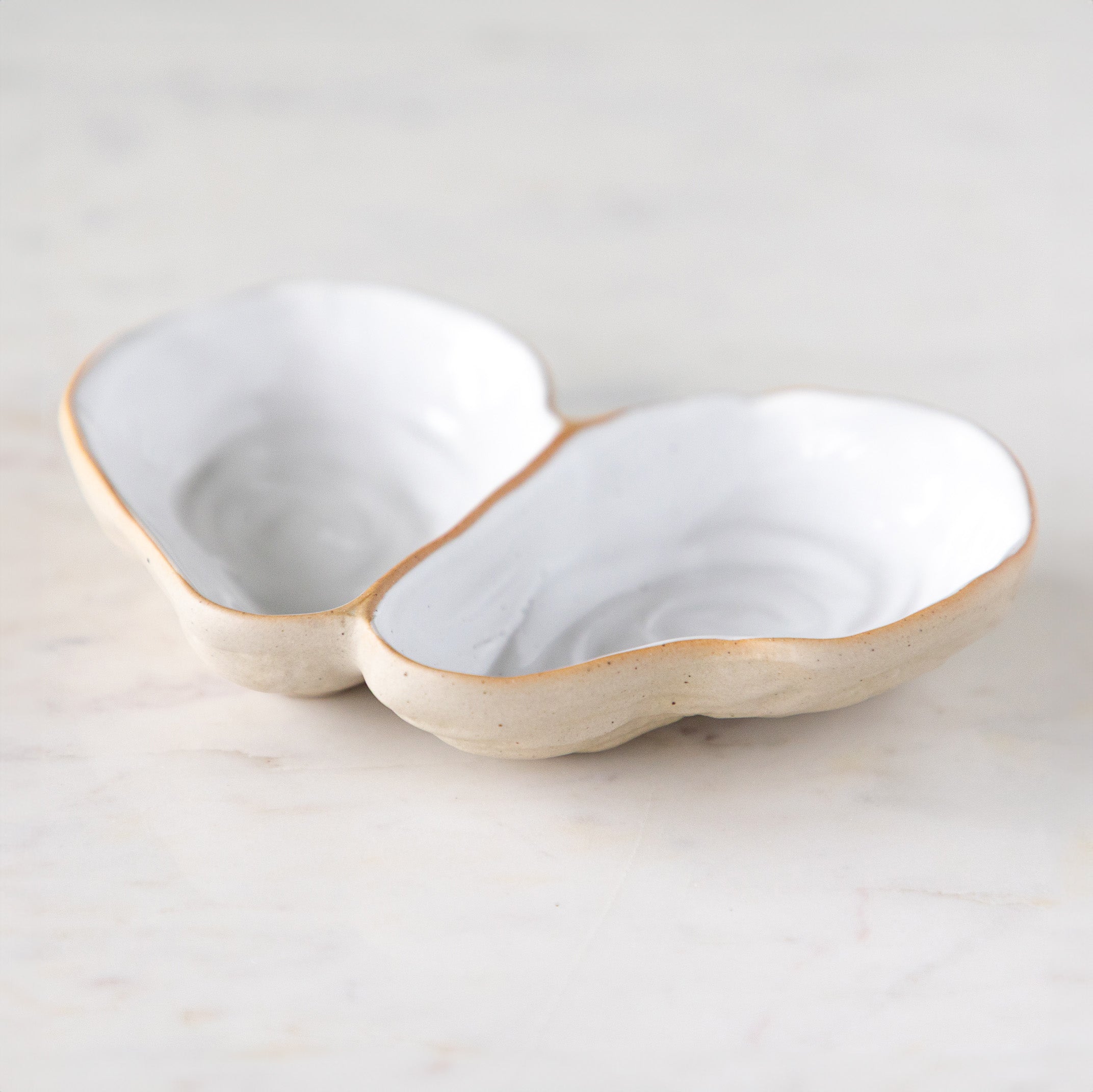 An open oyster shaped dish with white reflective glaze on the inside, on a marble table.