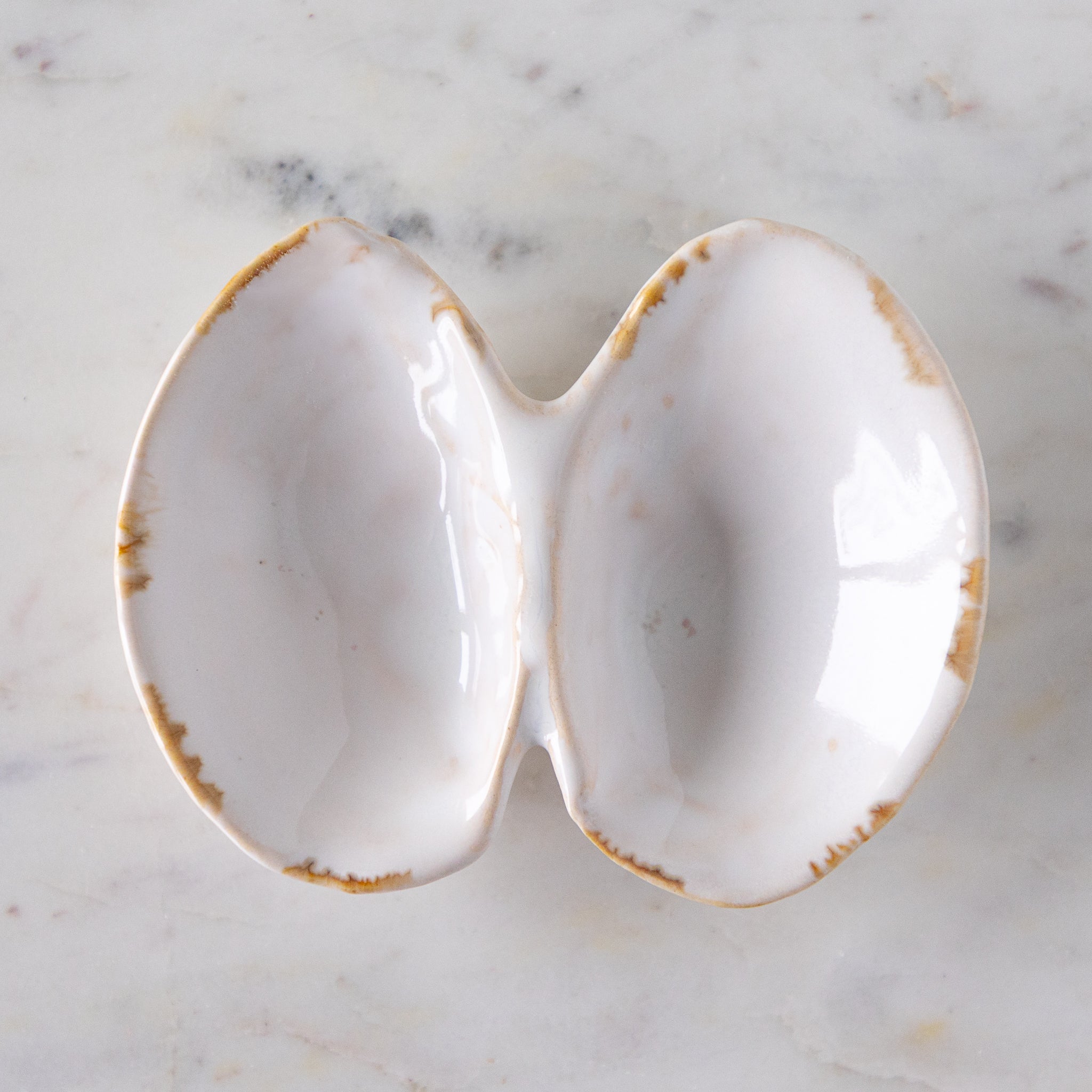 An open oyster shell shaped dish with white reflective glaze on the inside, on a marble table.