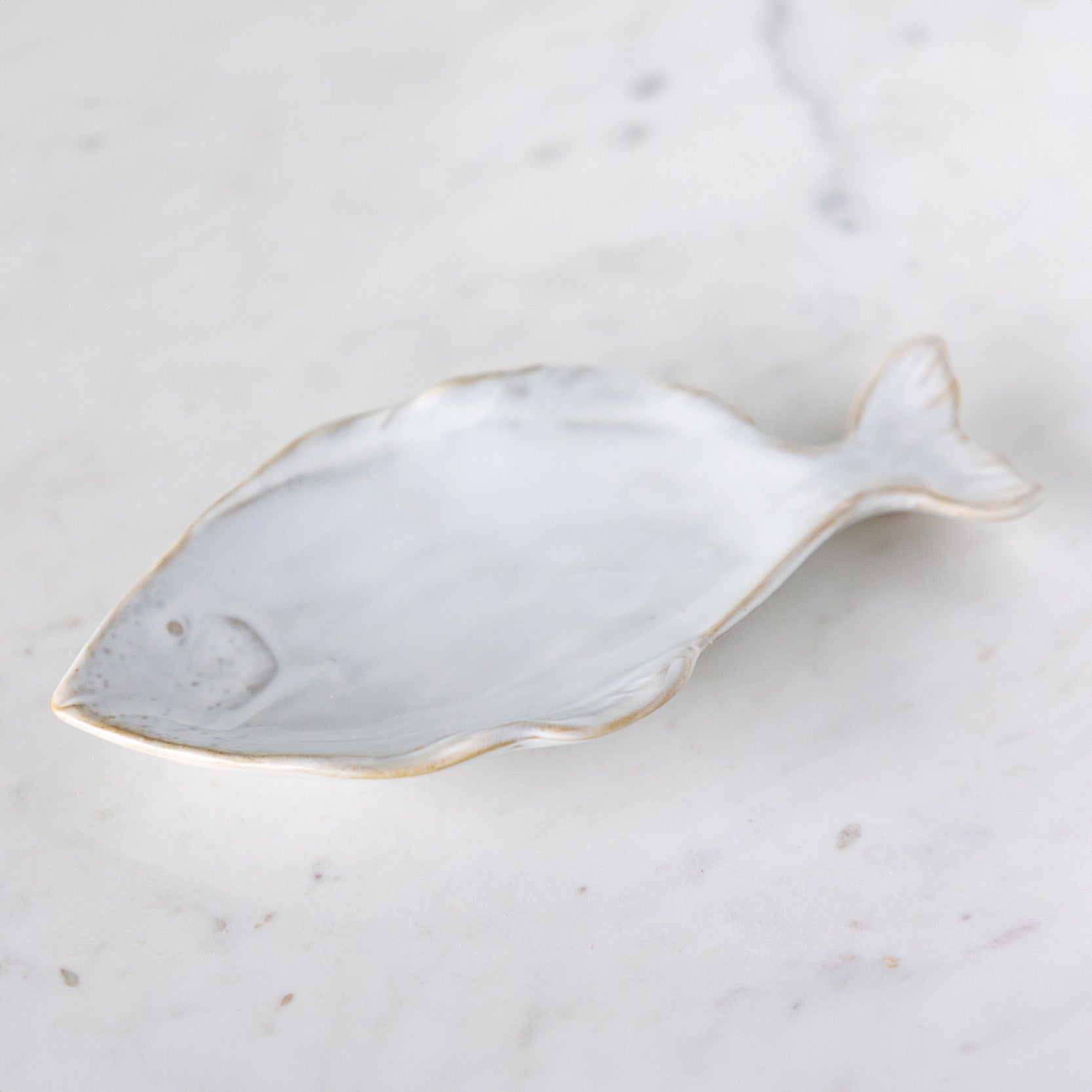 A stoneware, fish shaped dish with white reactive glaze, on a marble table.