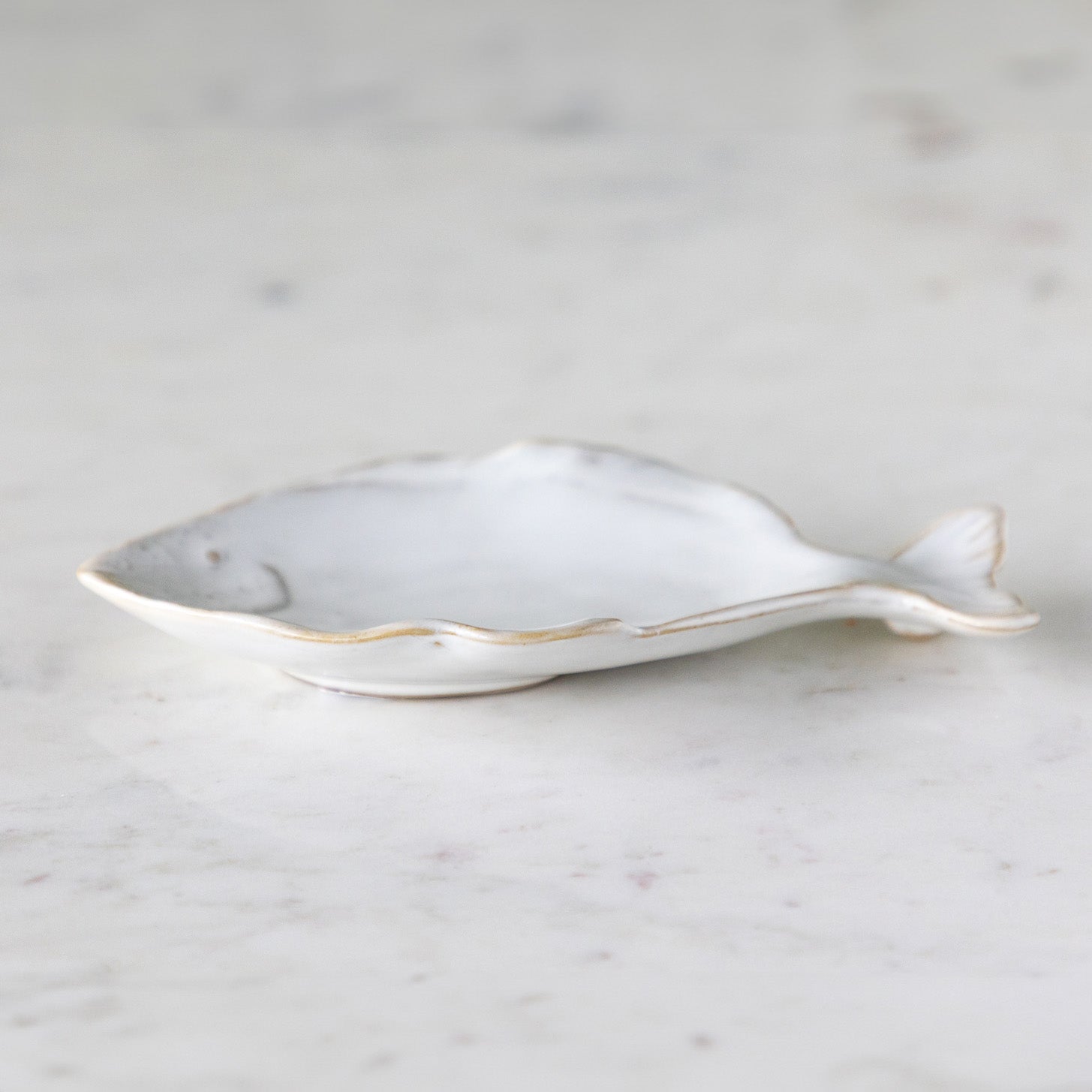 A stoneware, fish shaped dish with white reactive glaze, on a marble table.