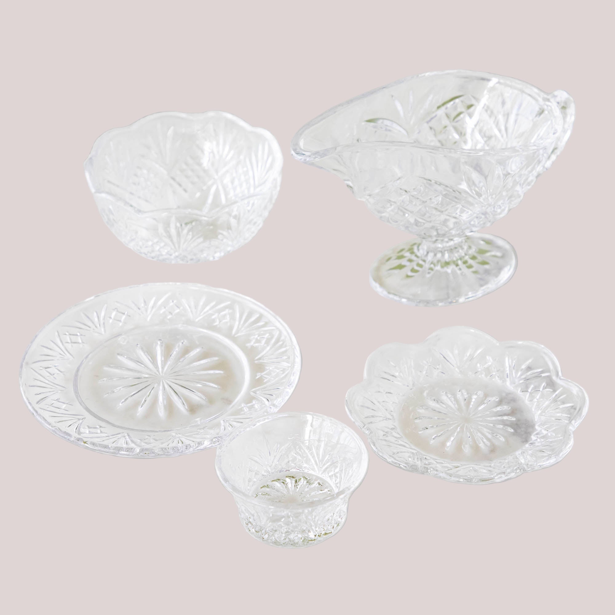 A set of clear crystal dinnerware on a marble surface, including various dishes and bowls with a geometric pattern.