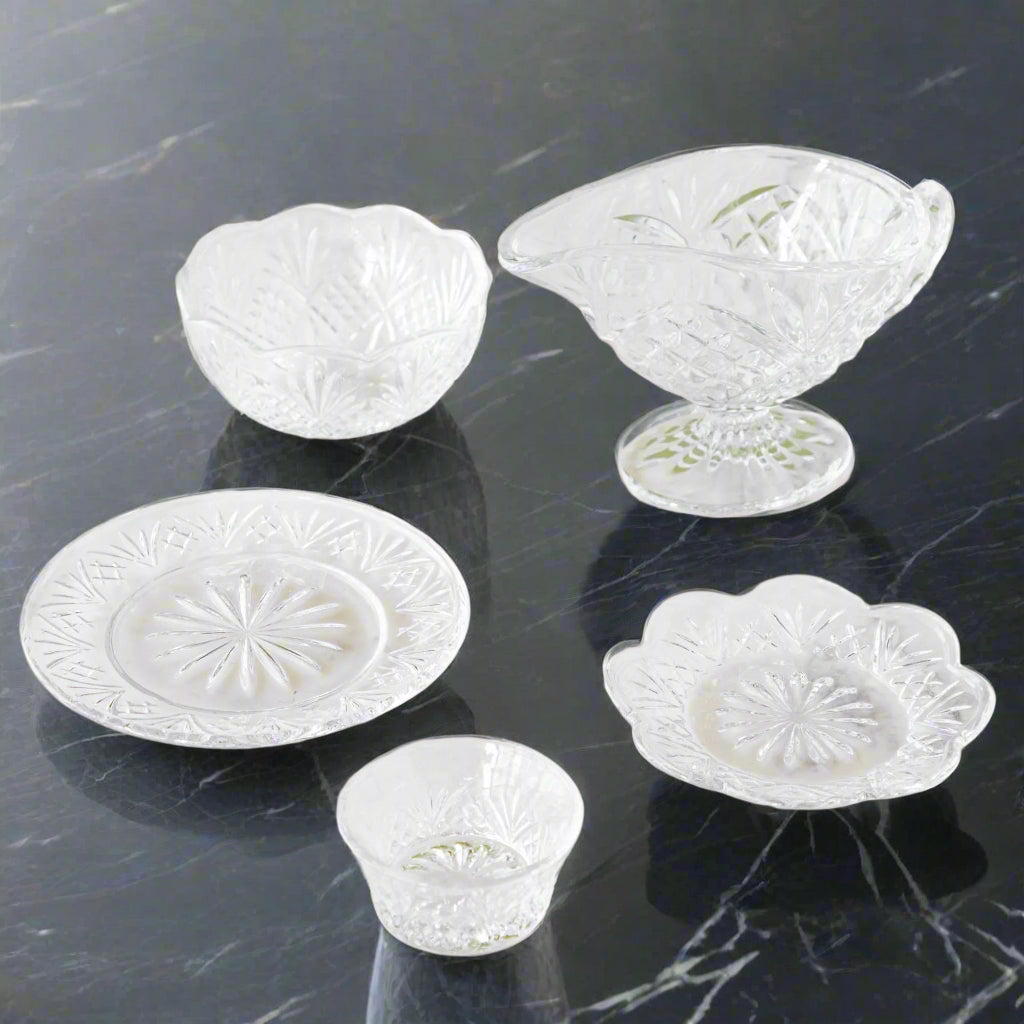 Clear glass pieces with etching including a gravy boat, small prep bowl, bowl with scalloped edge, small round plate, and round plate with a scalloped edge. 