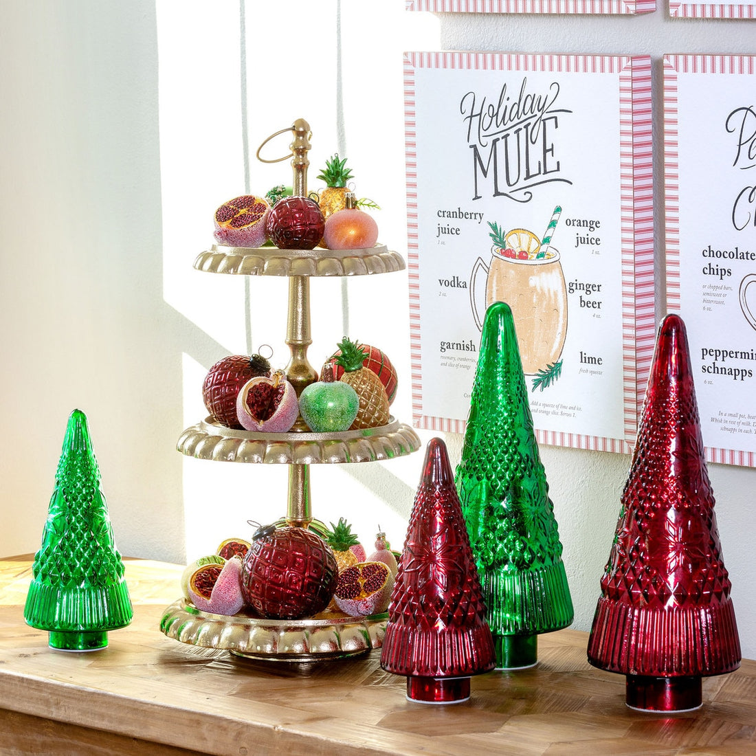 Decorative Christmas trees and a tiered fruit stand on a wooden surface with a &