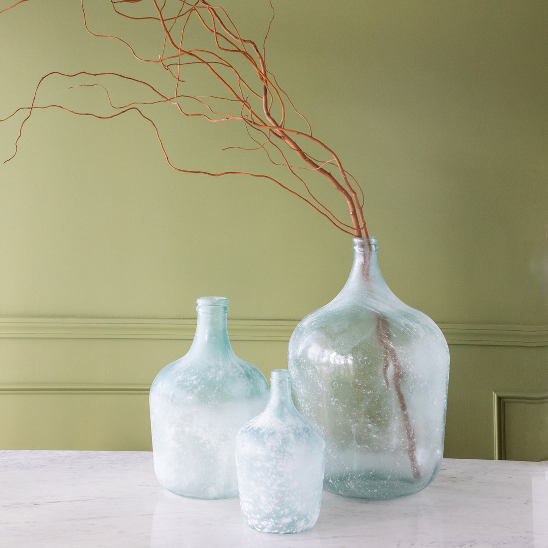 Frosted Seafoam Cellar Bottles in small, medium and large with branches coming out of the large bottle.