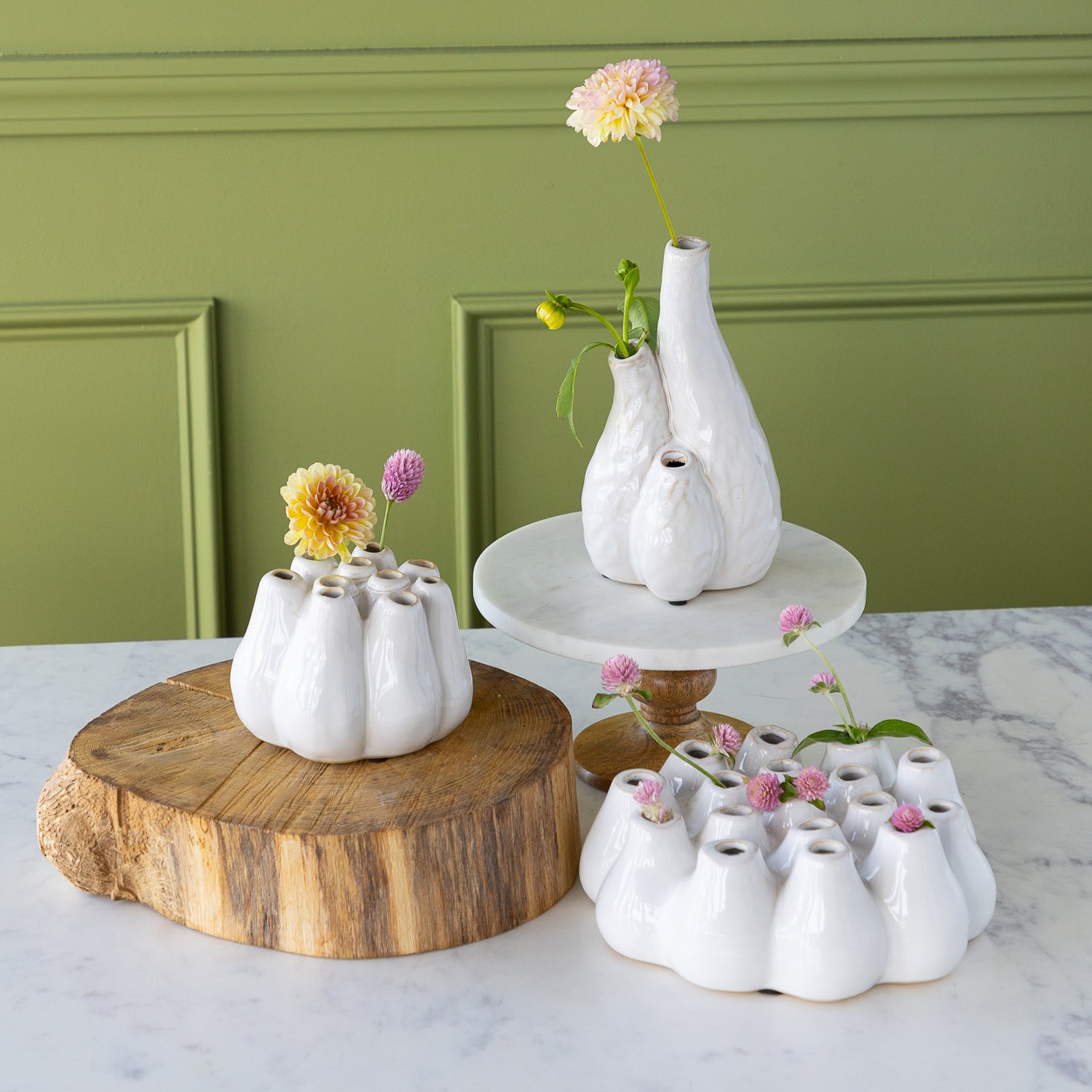 White ceramic vases with flowers on a marble surface against a green wall.