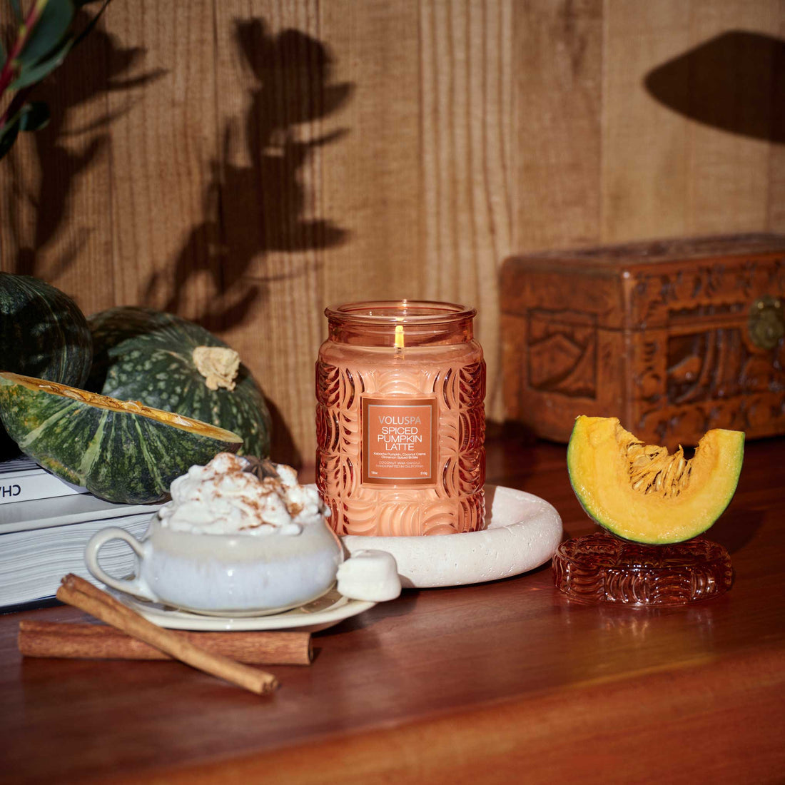 Candle with decorative pumpkins and a cup of hot chocolate on a wooden surface