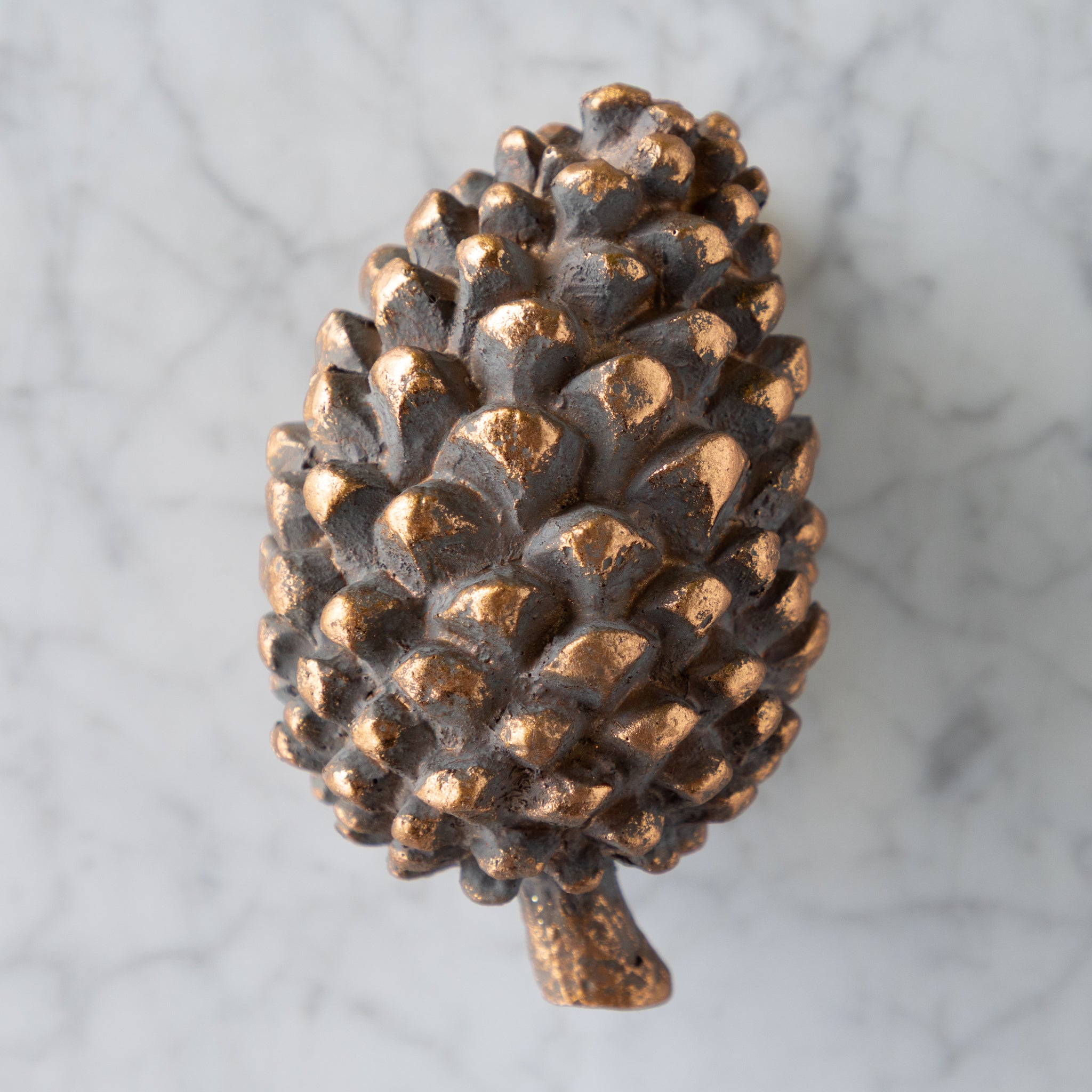 Bronze pine cone on a marble surface.