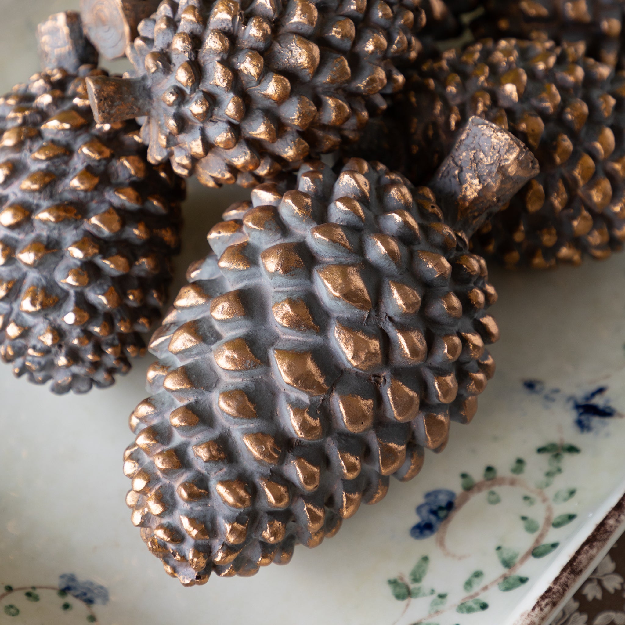 Bronze pinecones on a decorative plate with floral patterns.