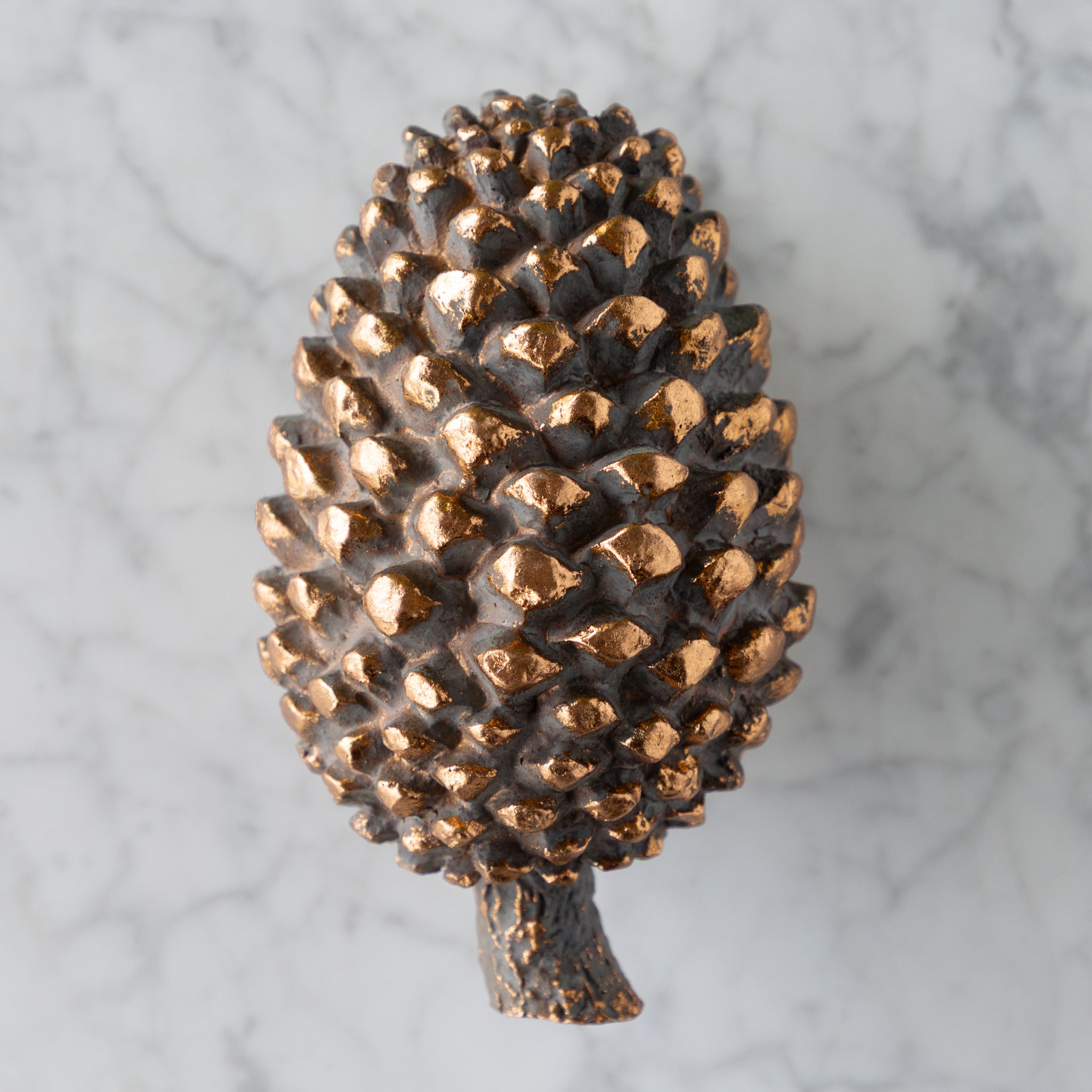 Bronze pine cone on a marble surface.