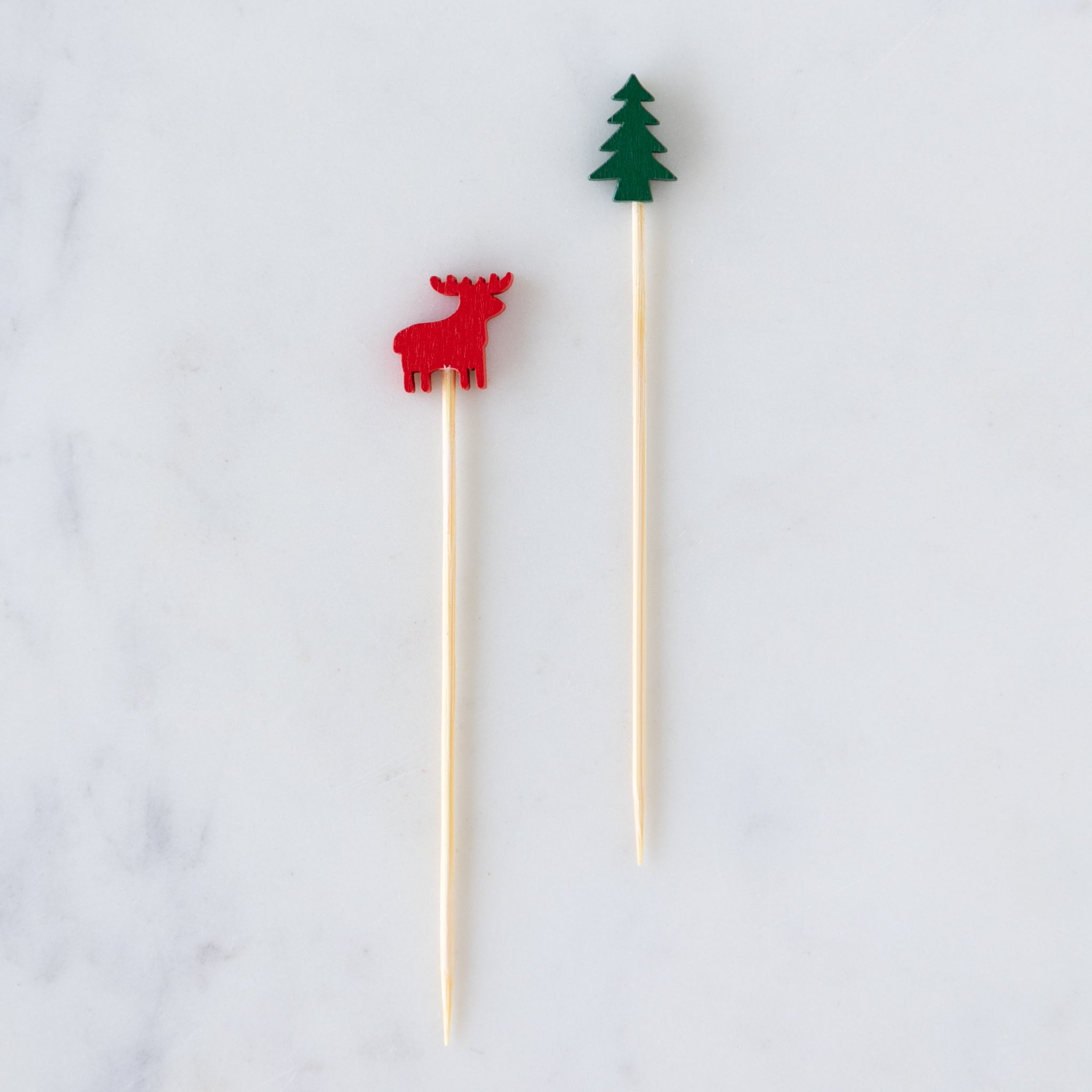 Two bamboo skewers with a red deer and green tree topper on a marble table.