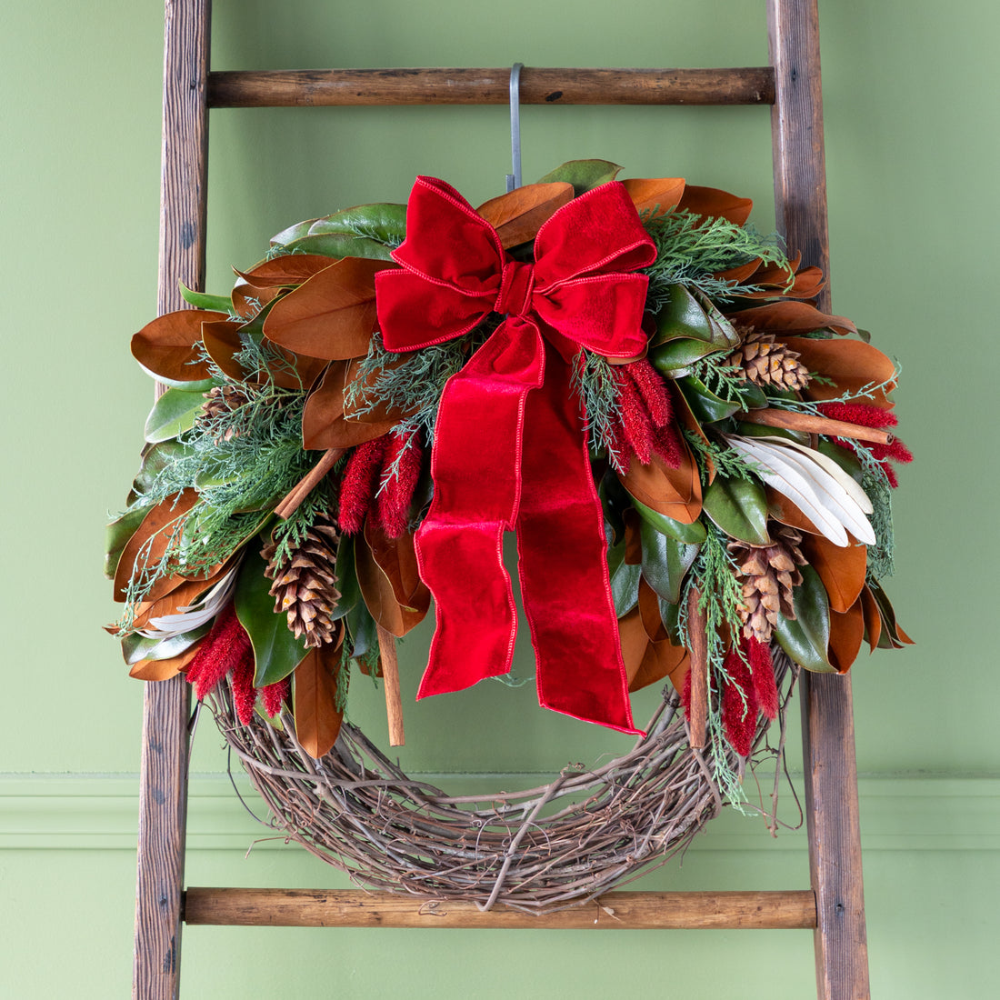 Decorative wreath with red bow on a wooden ladder against a green background