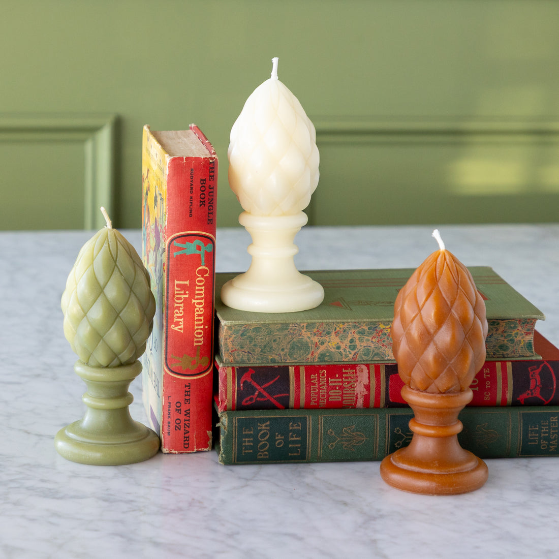Decorative candles on top of vintage books with a green wall background.