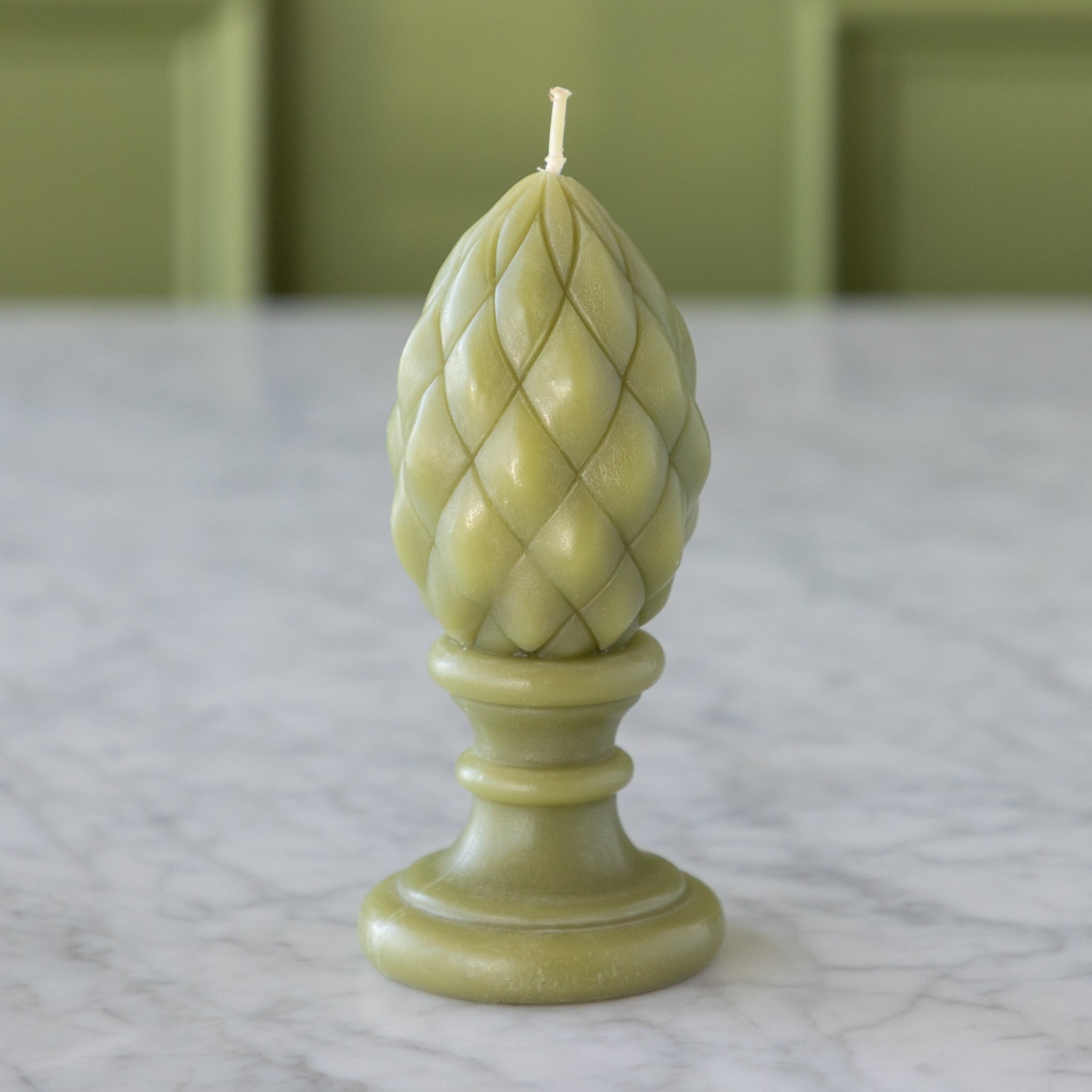 Decorative green candle with woven top on a marble surface.