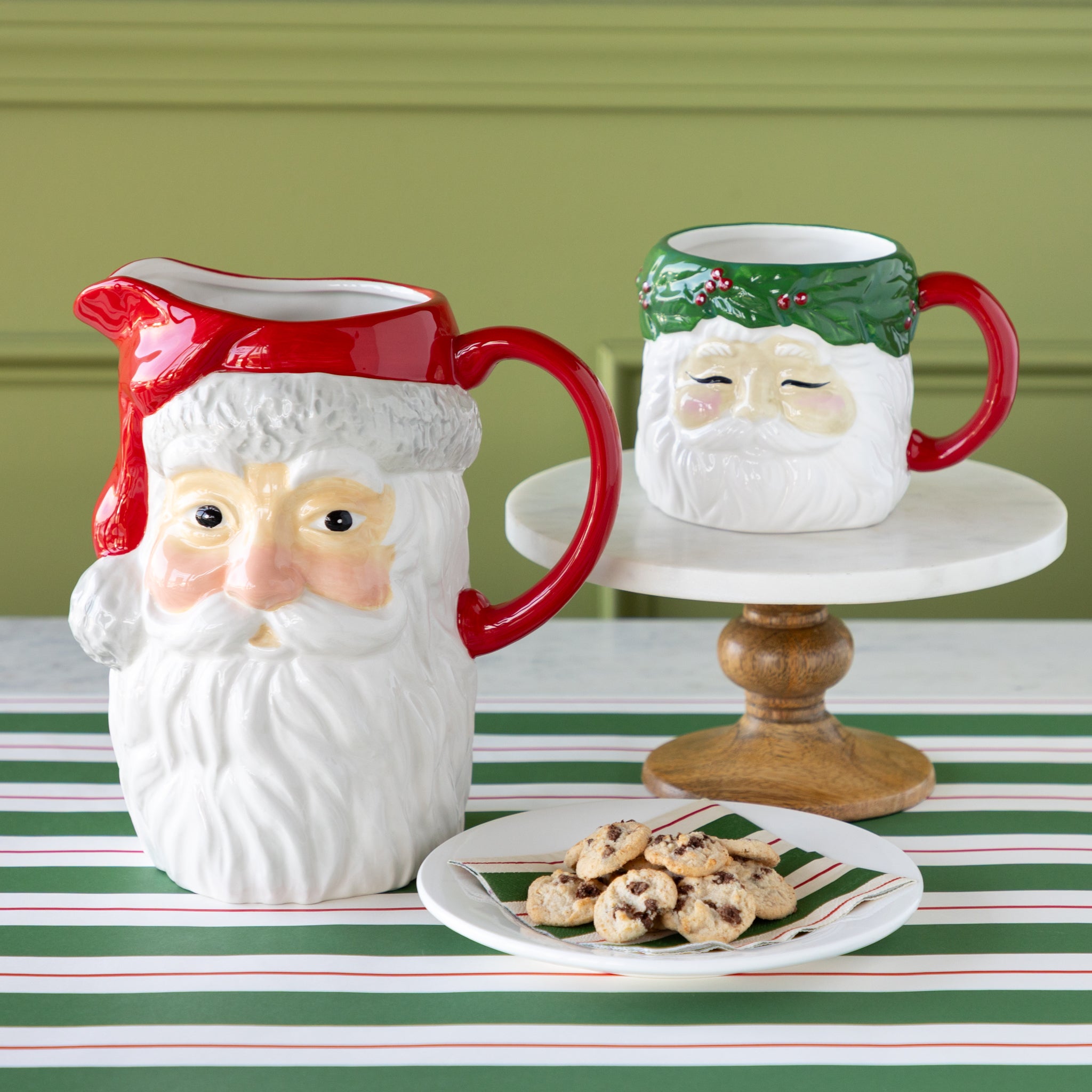 A ceramic pitcher and mug shaped like Santa Claus on a table with cookies.