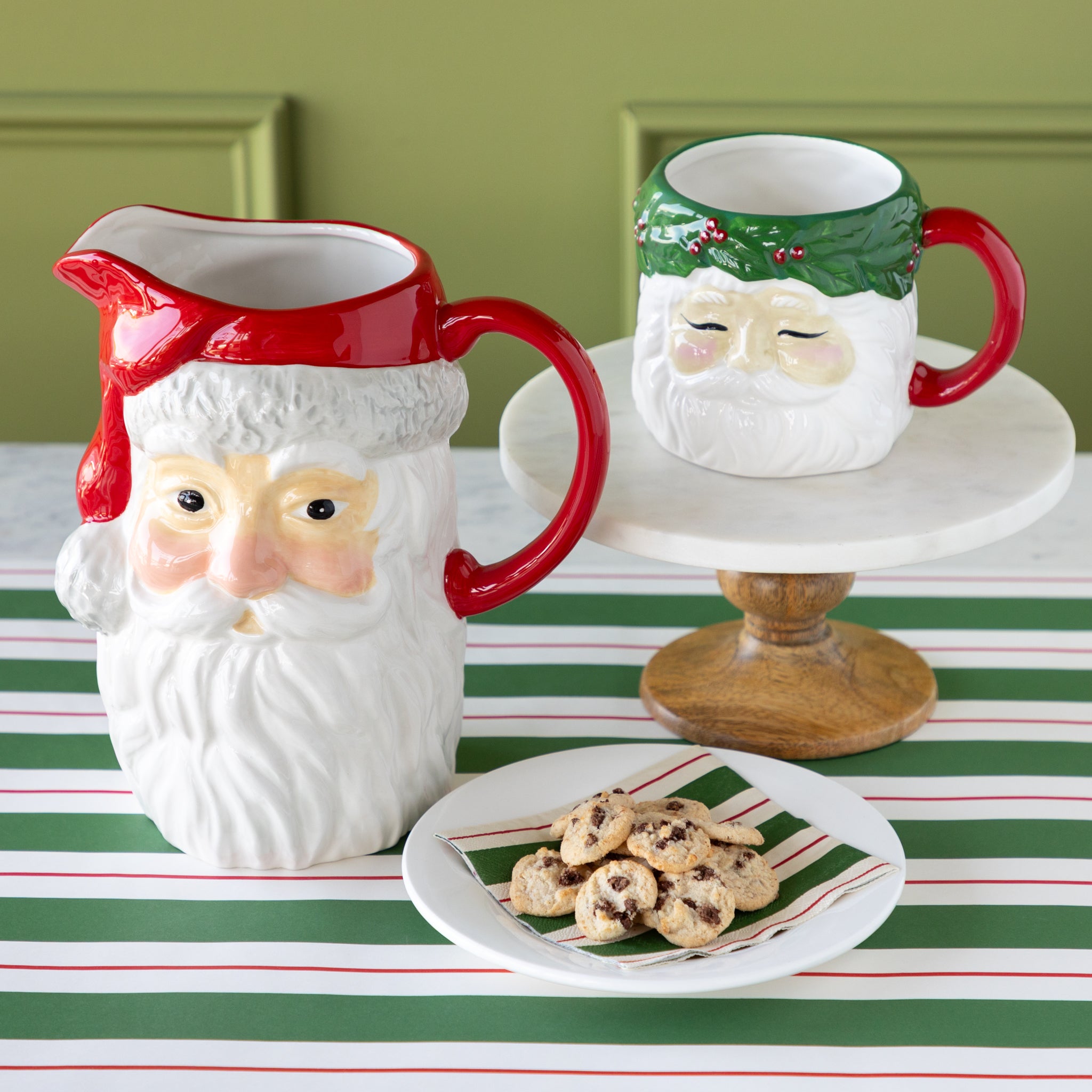 A ceramic pitcher and mug shaped like Santa Claus on a table with cookies.