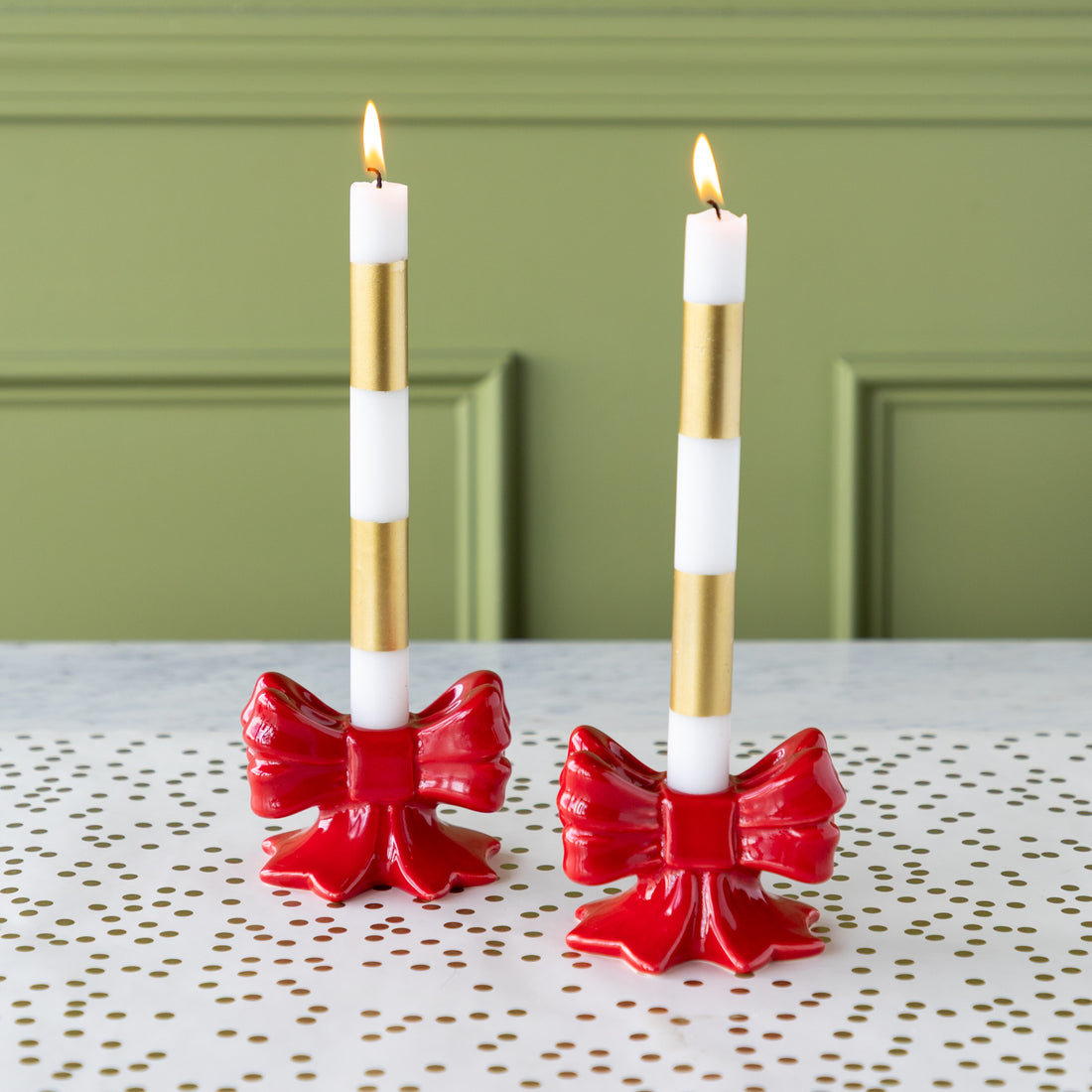 Two candle holders with red bows and gold and white taper candles on the Gold Confetti Runner.