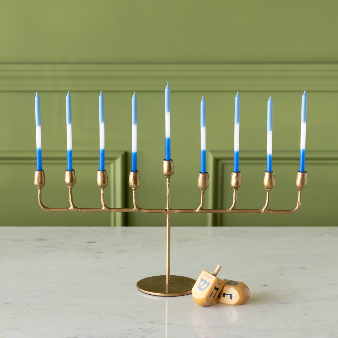 Gold menorah with blue and white menorah candles next to a dreidel against a green wall.