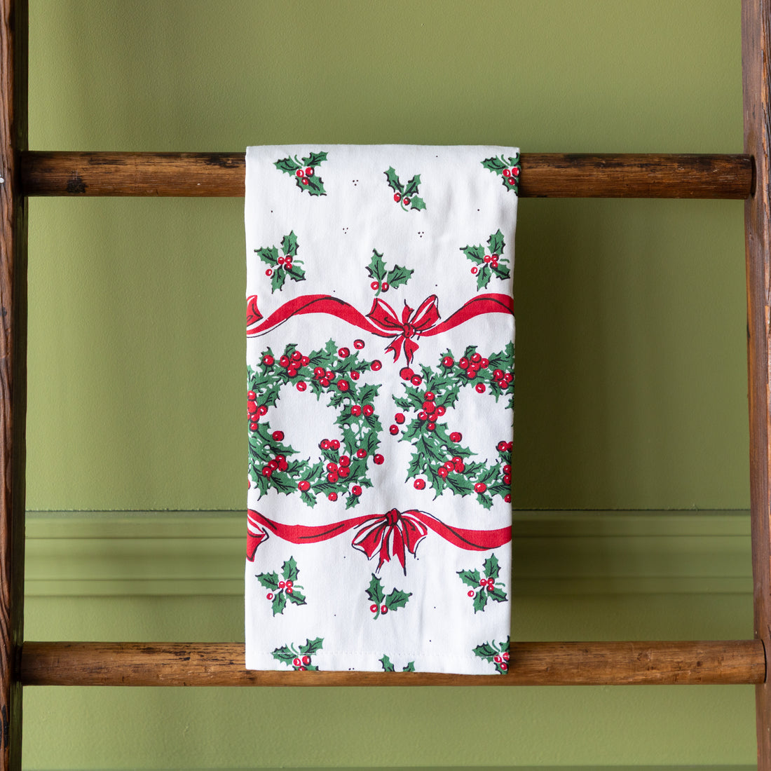 Vintage Holly Dishtowel hung over a wooden ladder.