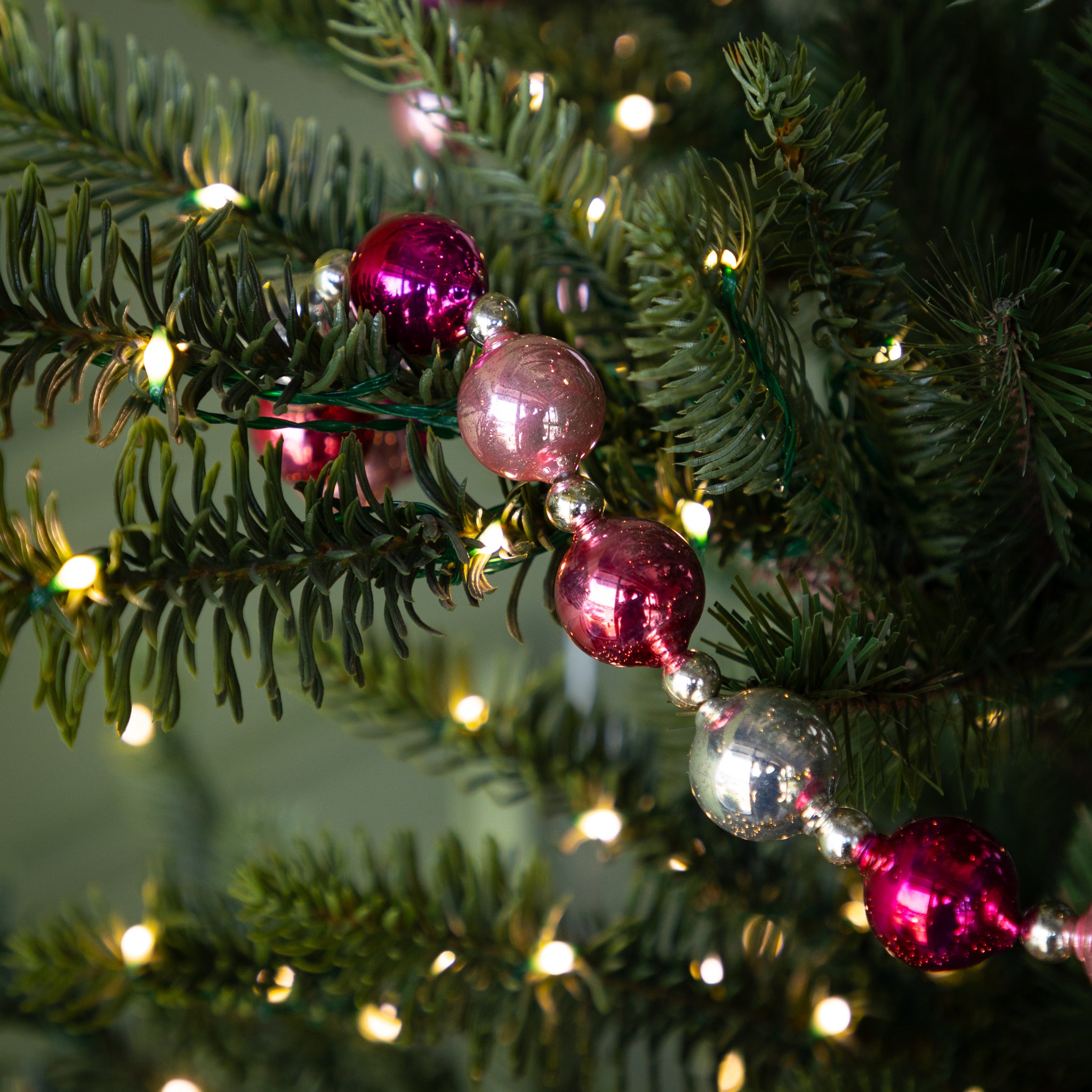 Close-up of a Christmas tree branch with a Pink & Silver Vintage Ornament Garland on it.
