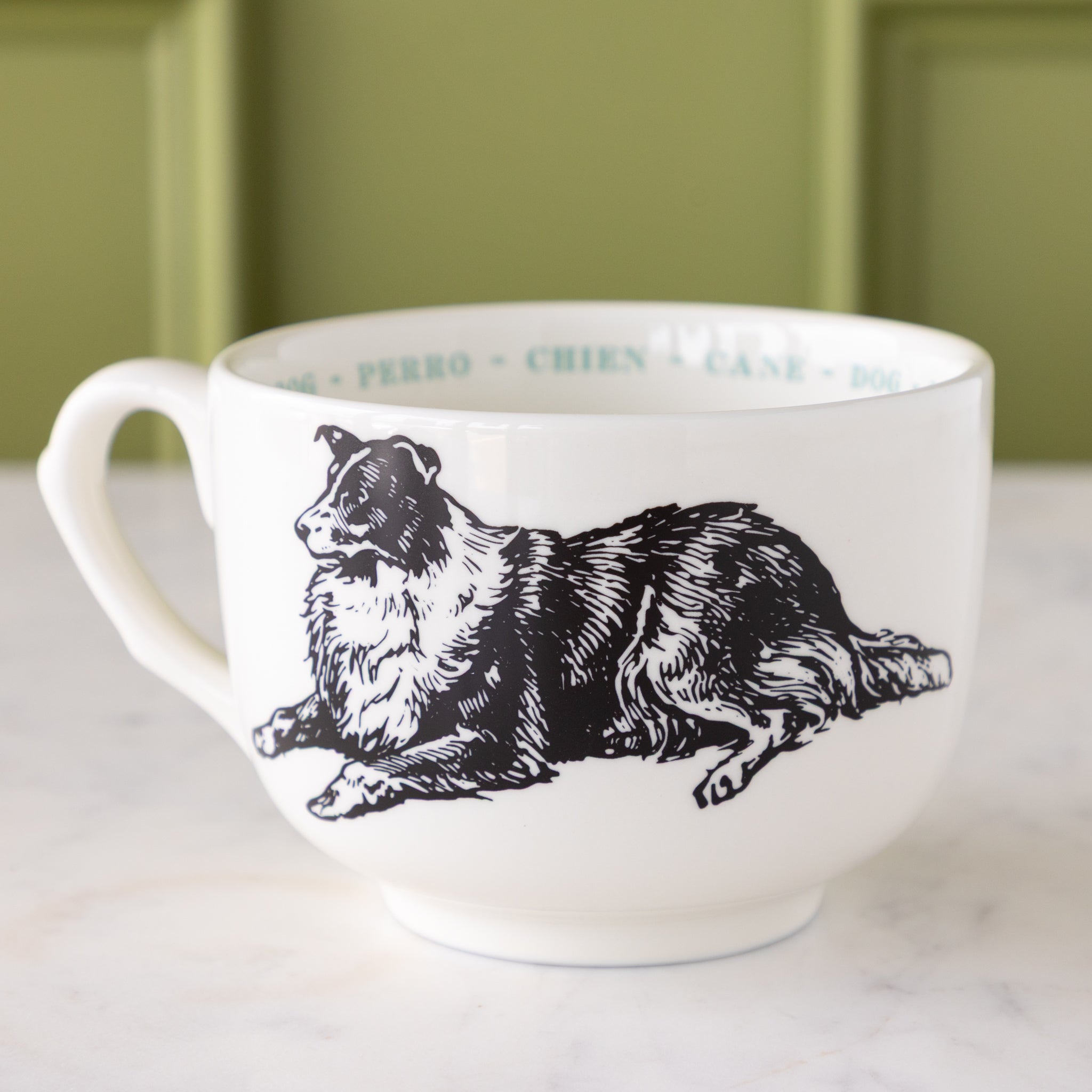 White mug with black dog illustration with "dog" in different languages in light blue text around the inside rim.