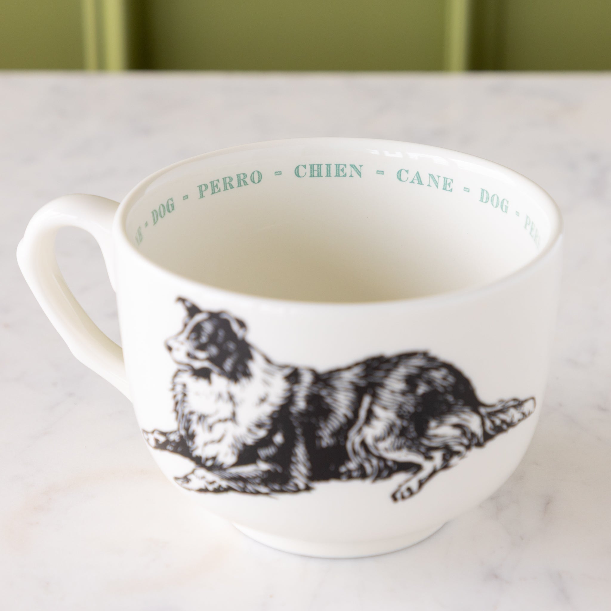 White mug with black dog illustration with "dog" in different languages in blue ext around the inside rim.