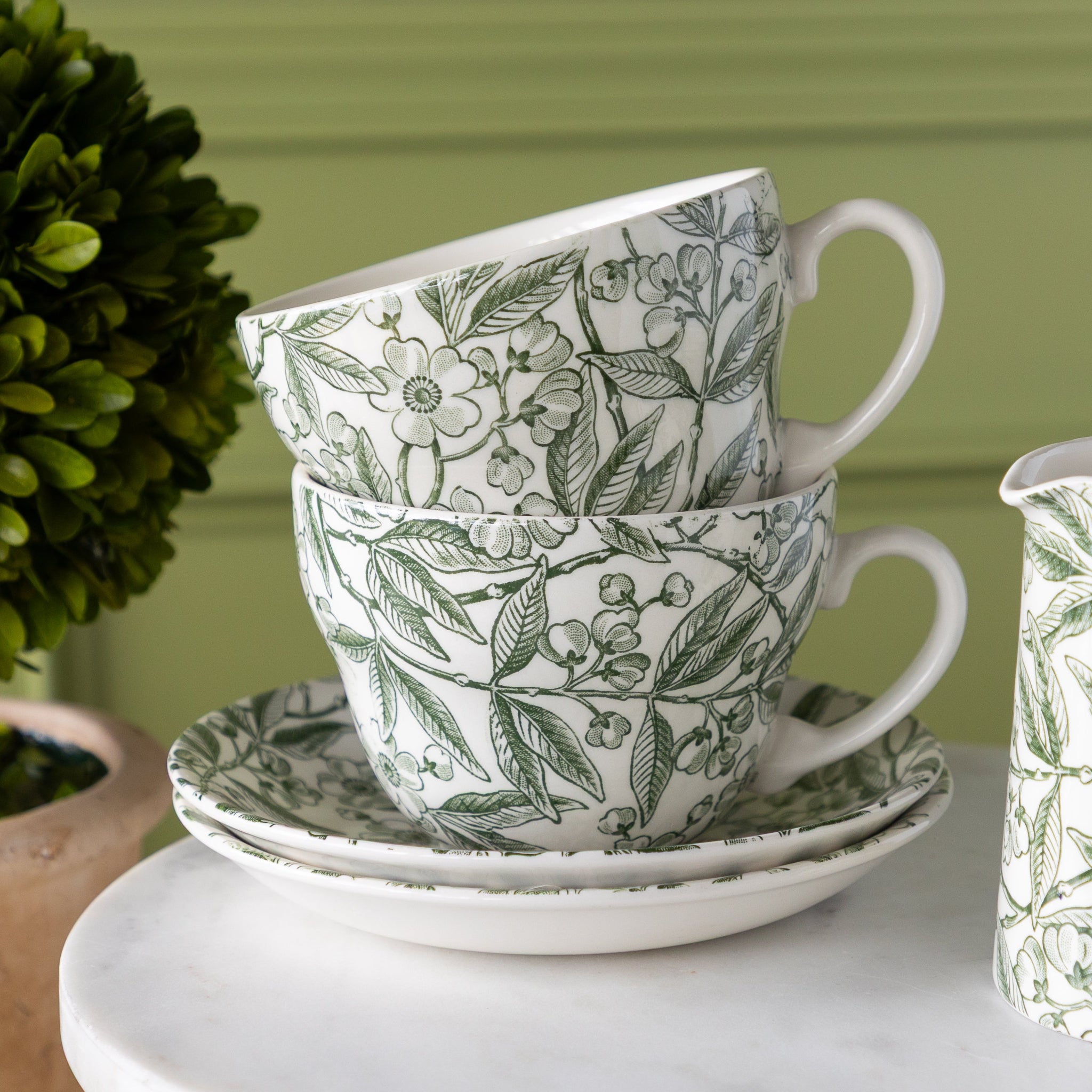 Two Burleigh Green Prunus Cups stacked on top of two saucers on a pedestal.