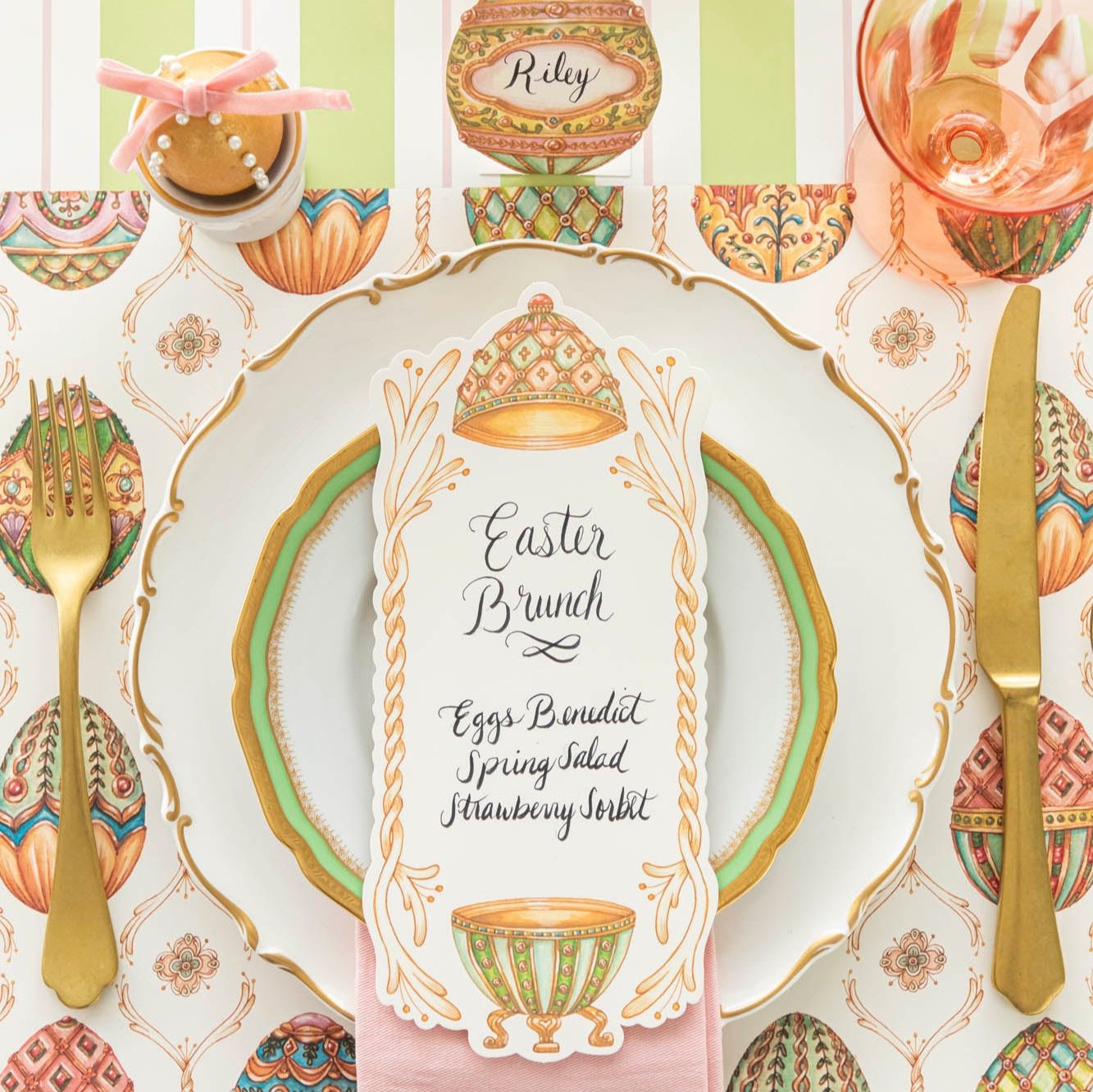 An elegant, Faberge Egg themed table setting, featuring the Exquisite Egg Hunt Placemat, Exquisite Egg Table Card with a menu written on it, and the Green & Pink Awning Stripe Runner underneath.