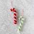 Two felt candy cane-shaped ornaments in red and seafoam on a marble surface.