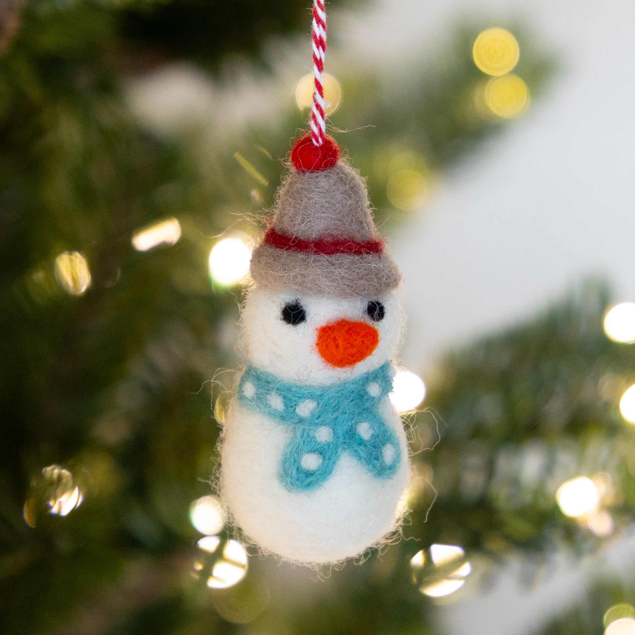 Felt snowman ornament hanging on a Christmas tree with blurred lights in the background.