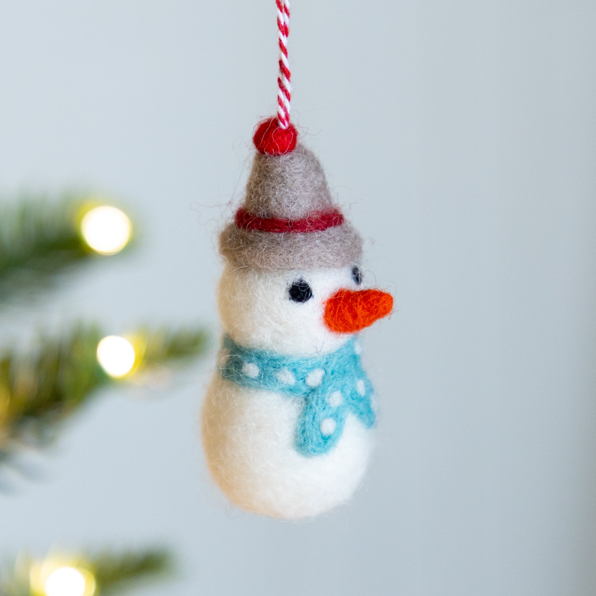 Felt snowman ornament with a red hat and blue scarf hanging against a light background.