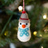 Felt snowman ornament hanging on a Christmas tree with blurred lights in the background.