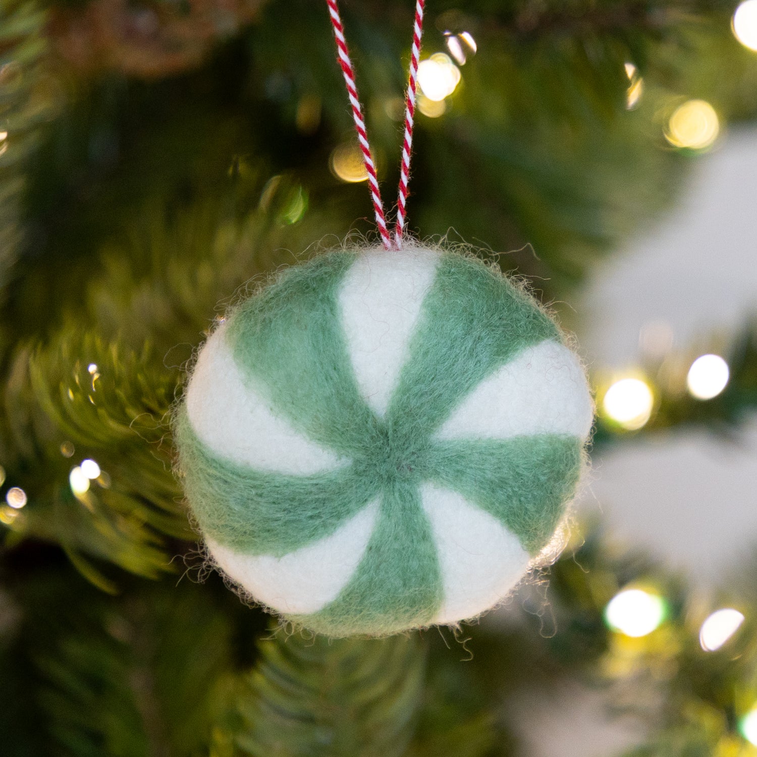Felt ornament shaped like a peppermint candy in seafoam and white on a Christmas tree.