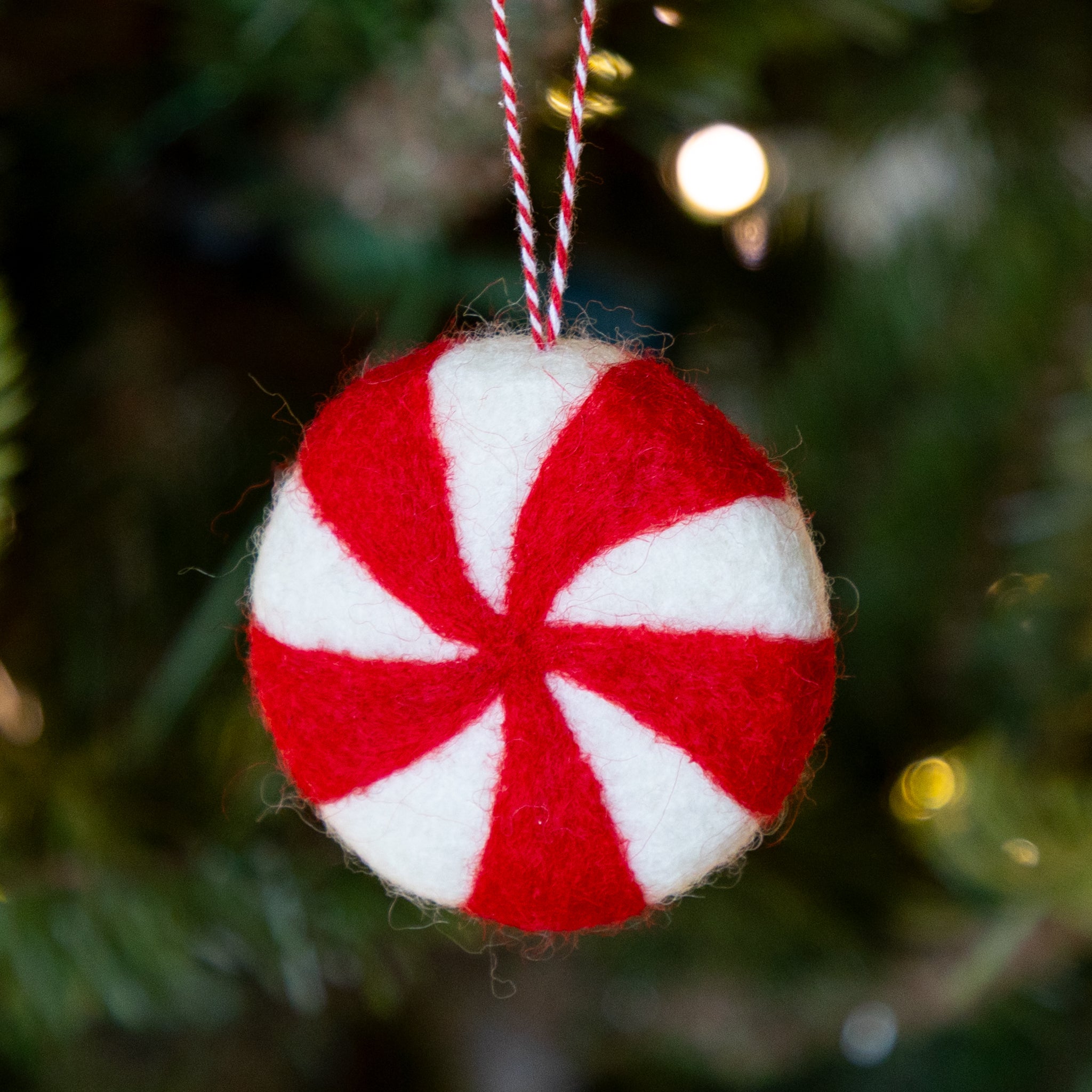 Felt ornament shaped like a peppermint candy in red and white on a Christmas tree.