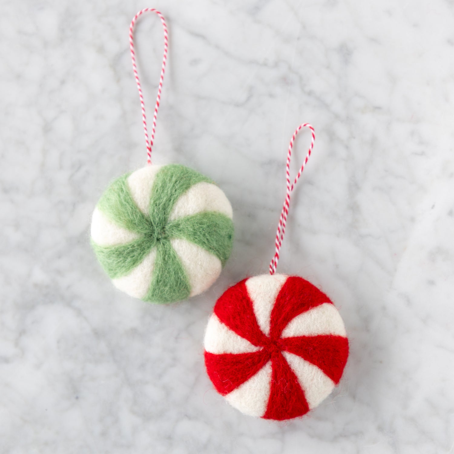 Two felt peppermint candy ornaments in red and seafoam on a marble table.
