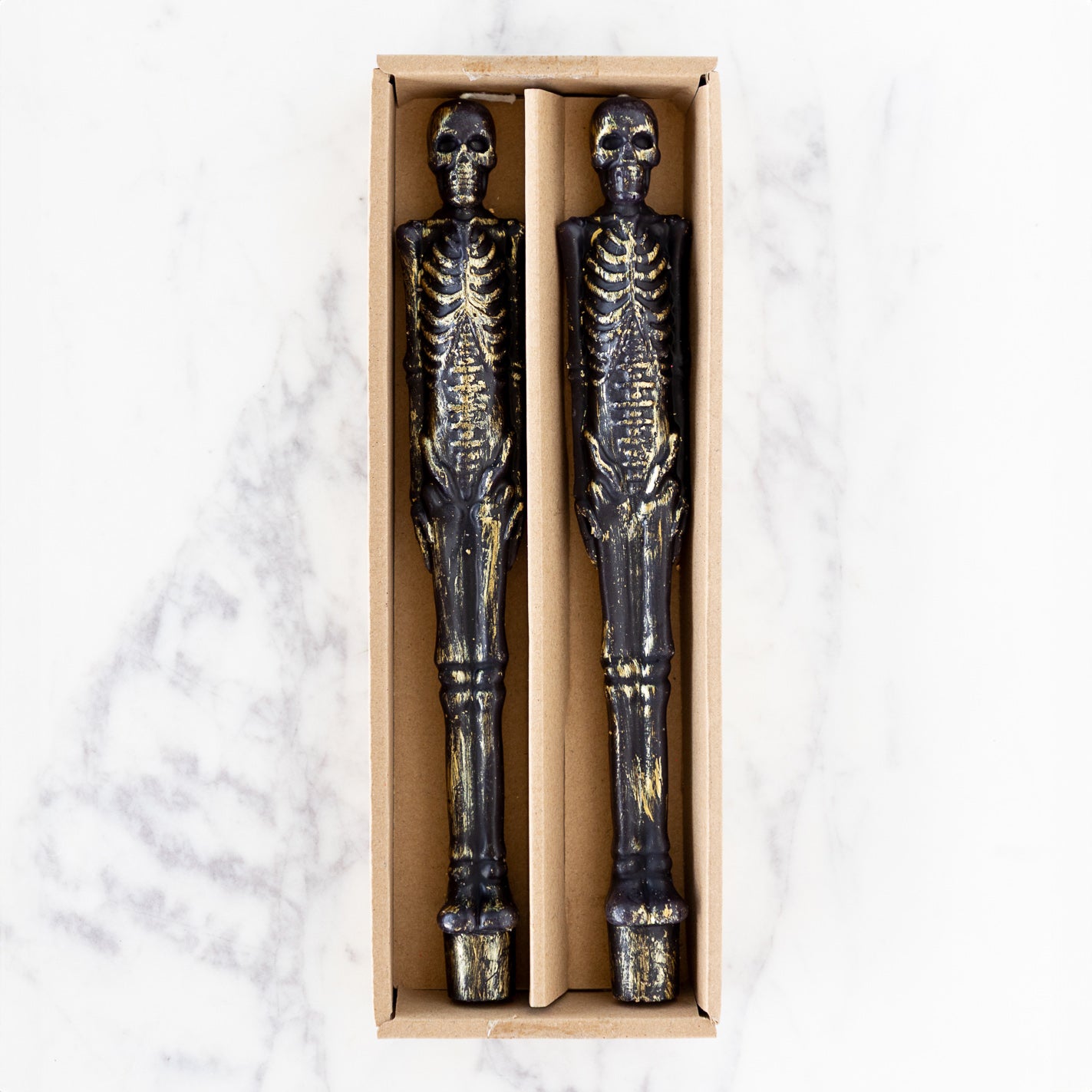 Two Skeleton Taper Candles in a box on a white surface.