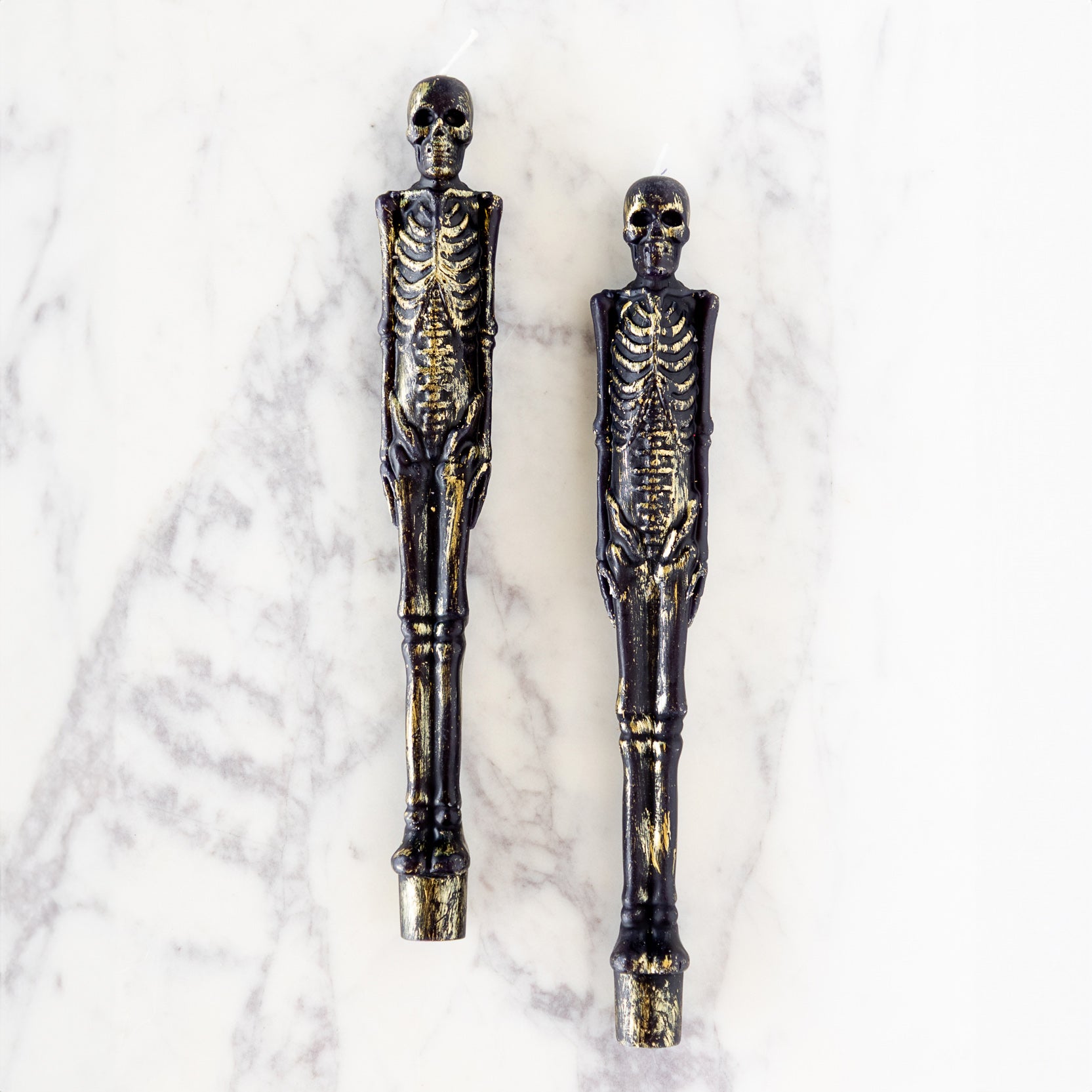 Two Skeleton Taper Candles on marble table.