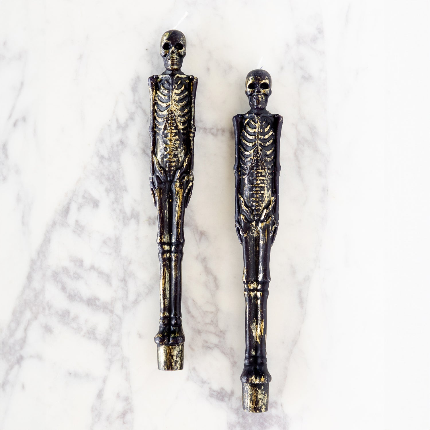 Two Skeleton Taper Candles on marble table.
