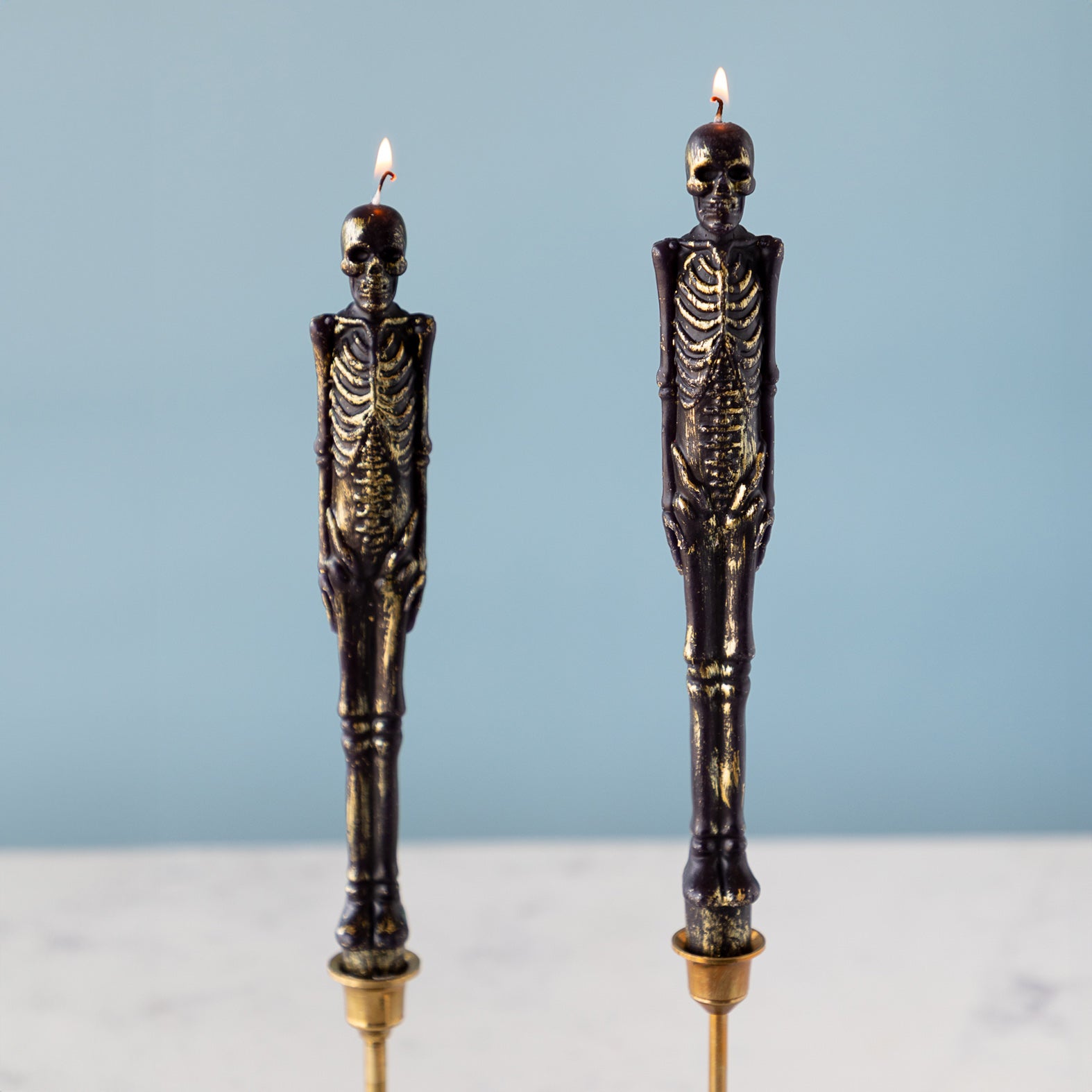Two lit skeleton taper candles against a blue background.