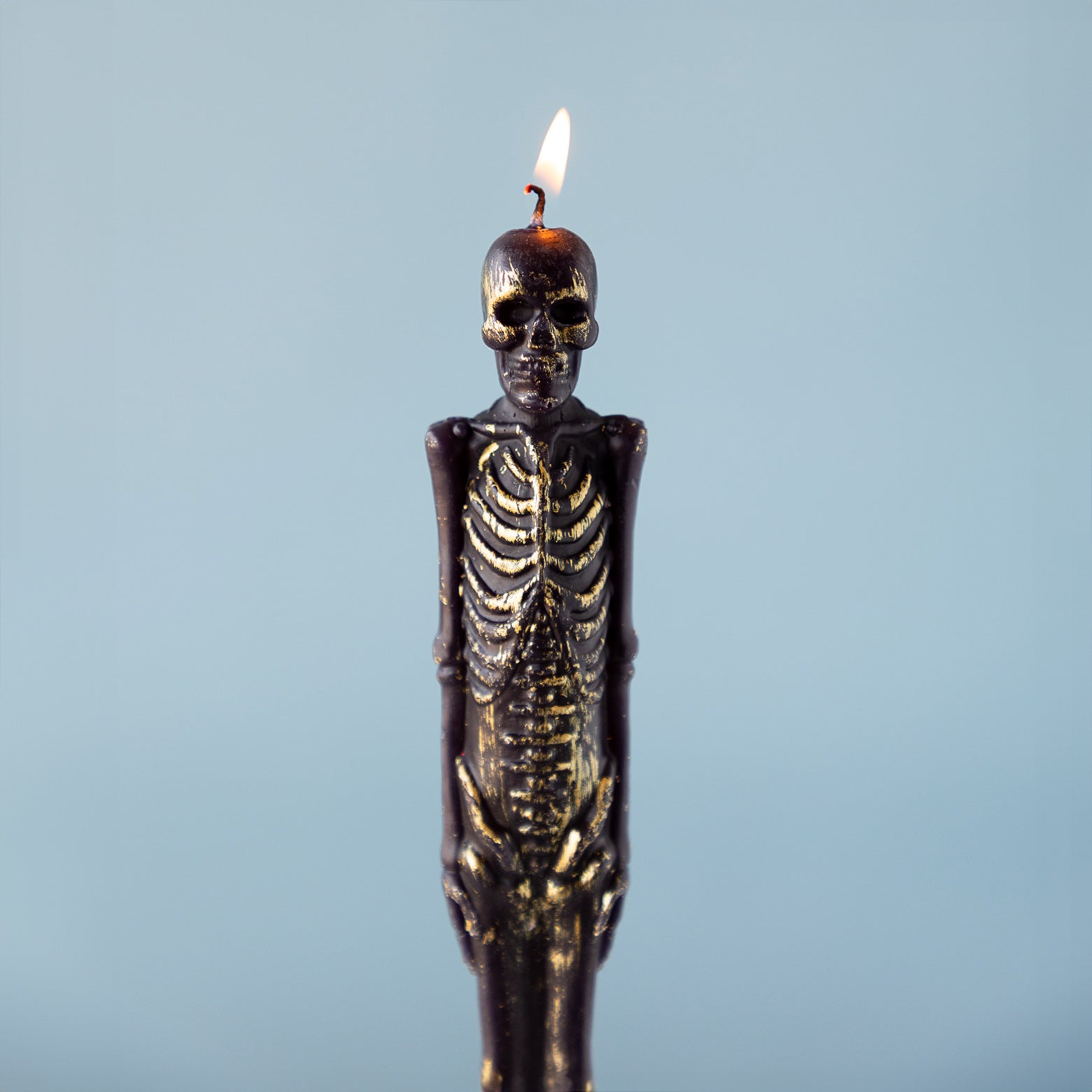 A lit Skeleton Taper Candle against a blue background.