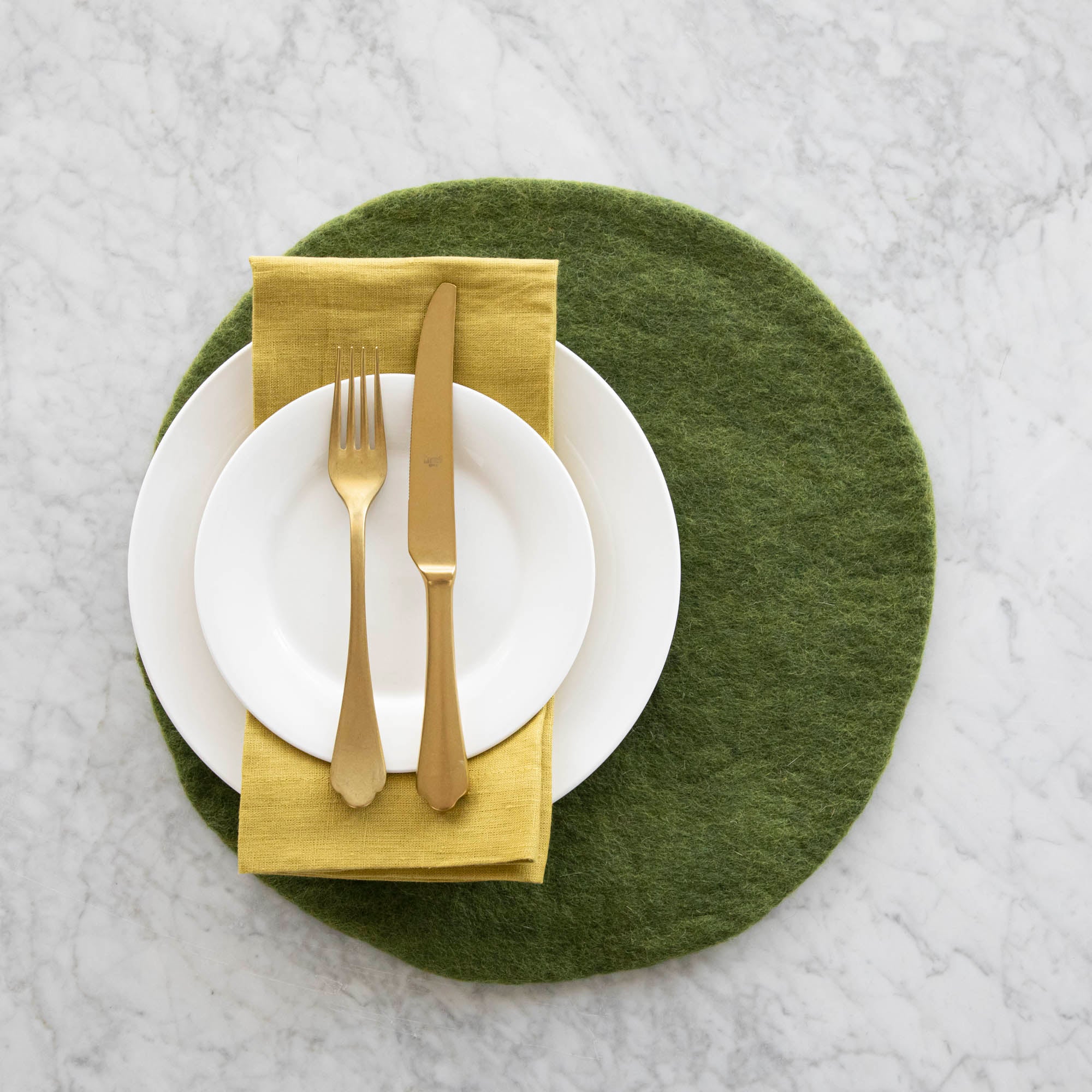 The Forest Green Felt Placemat under a place setting with two white plates, a gold a napkin and gold fork and knife atop.